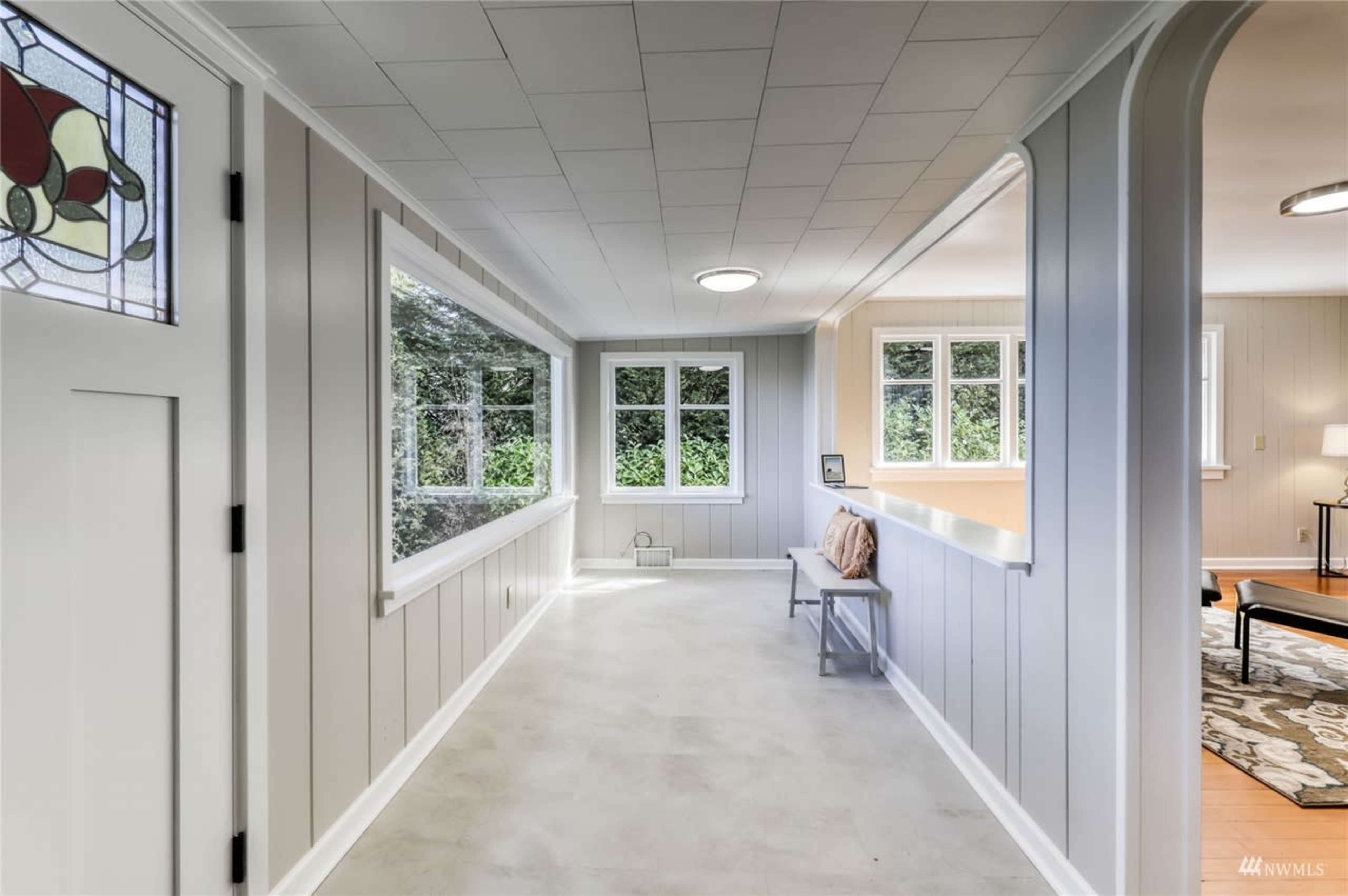 A bright, narrow hallway with a bench and large windows that provide views of greenery outside.