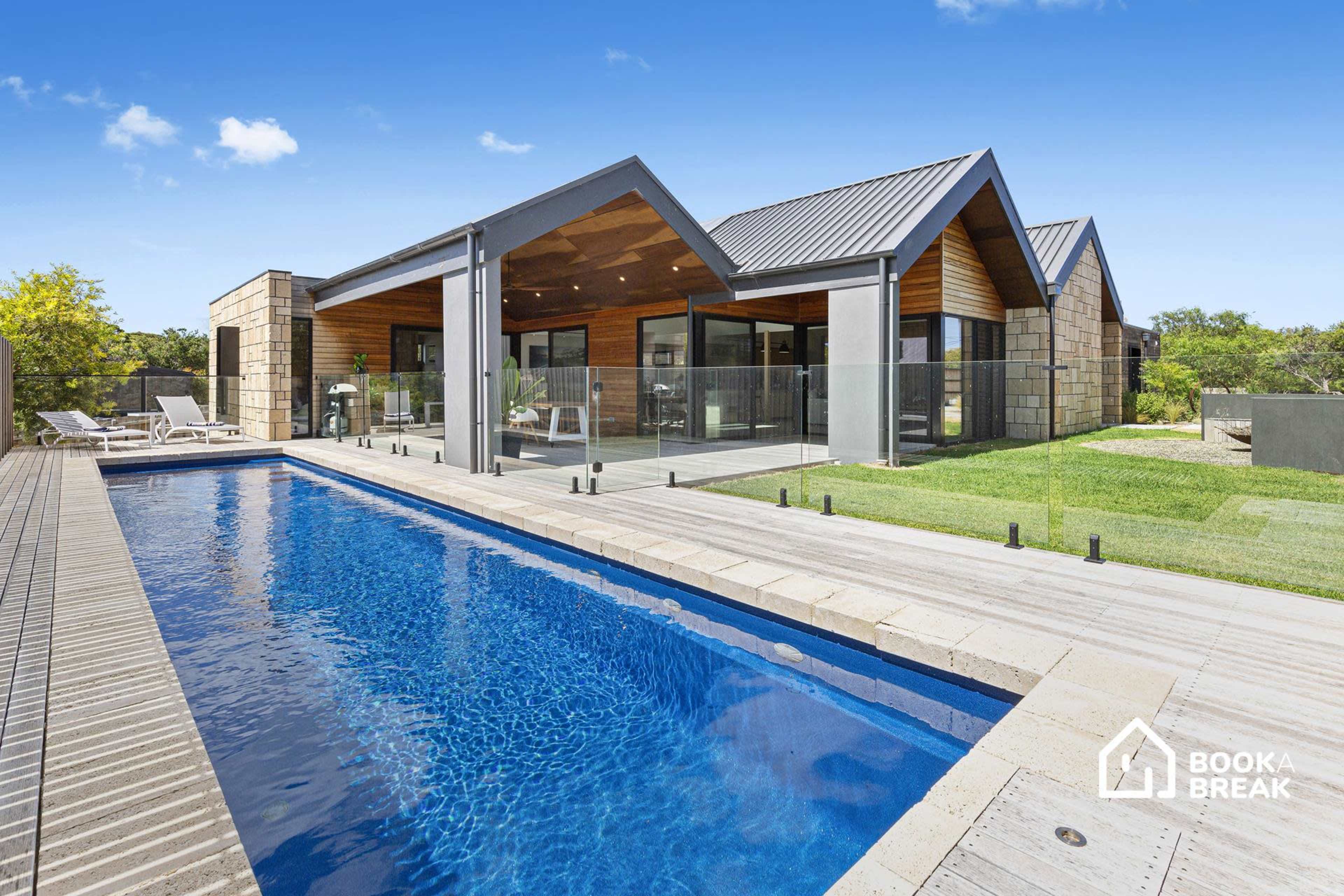 A modern house with a swimming pool and a landscaped yard under a clear blue sky.