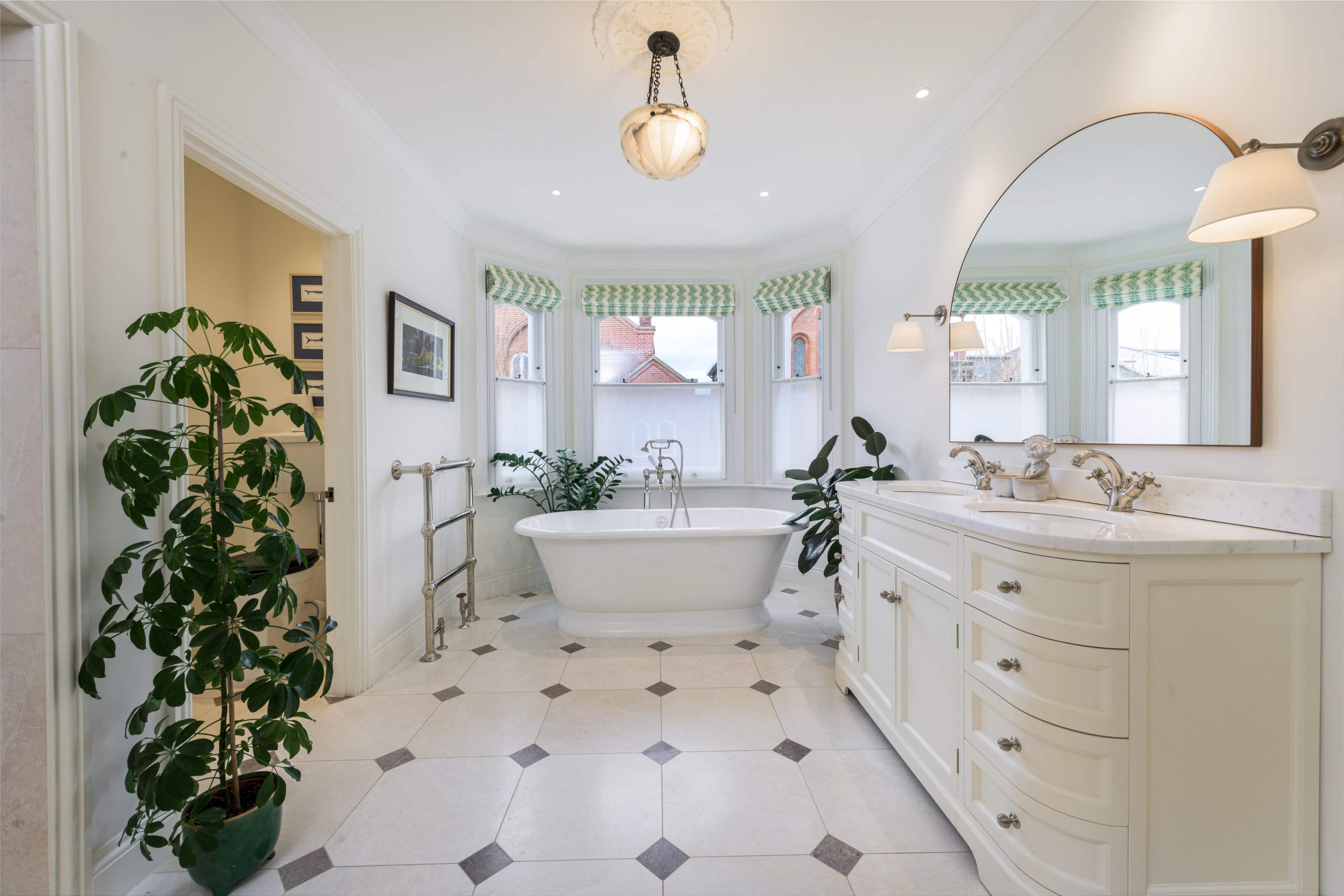 The spacious bathroom features a freestanding tub, a double sink vanity, and large windows with green patterned shades.