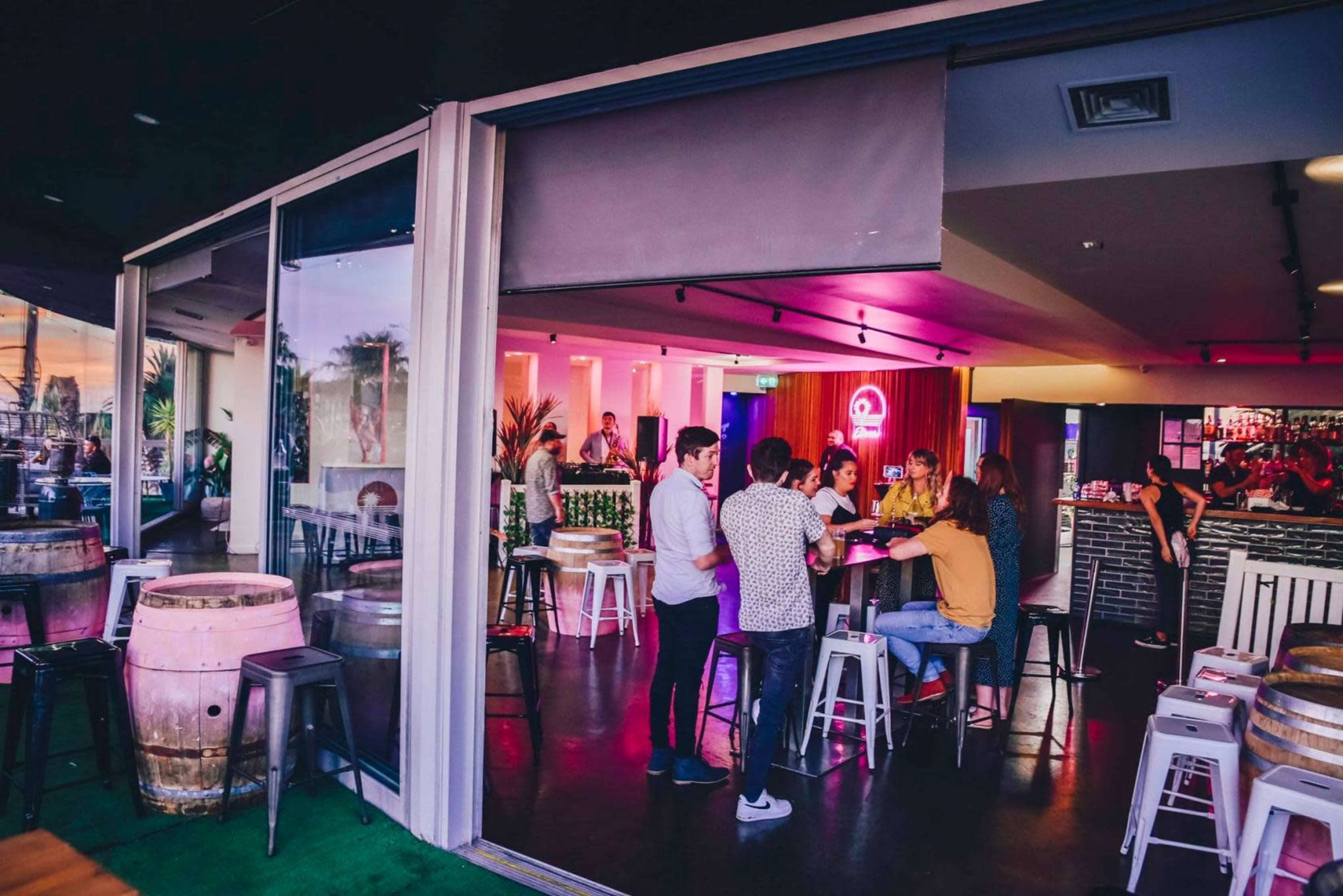 A social gathering takes place in a modern bar, featuring high tables and a well-lit interior with patrons engaging at the counter.