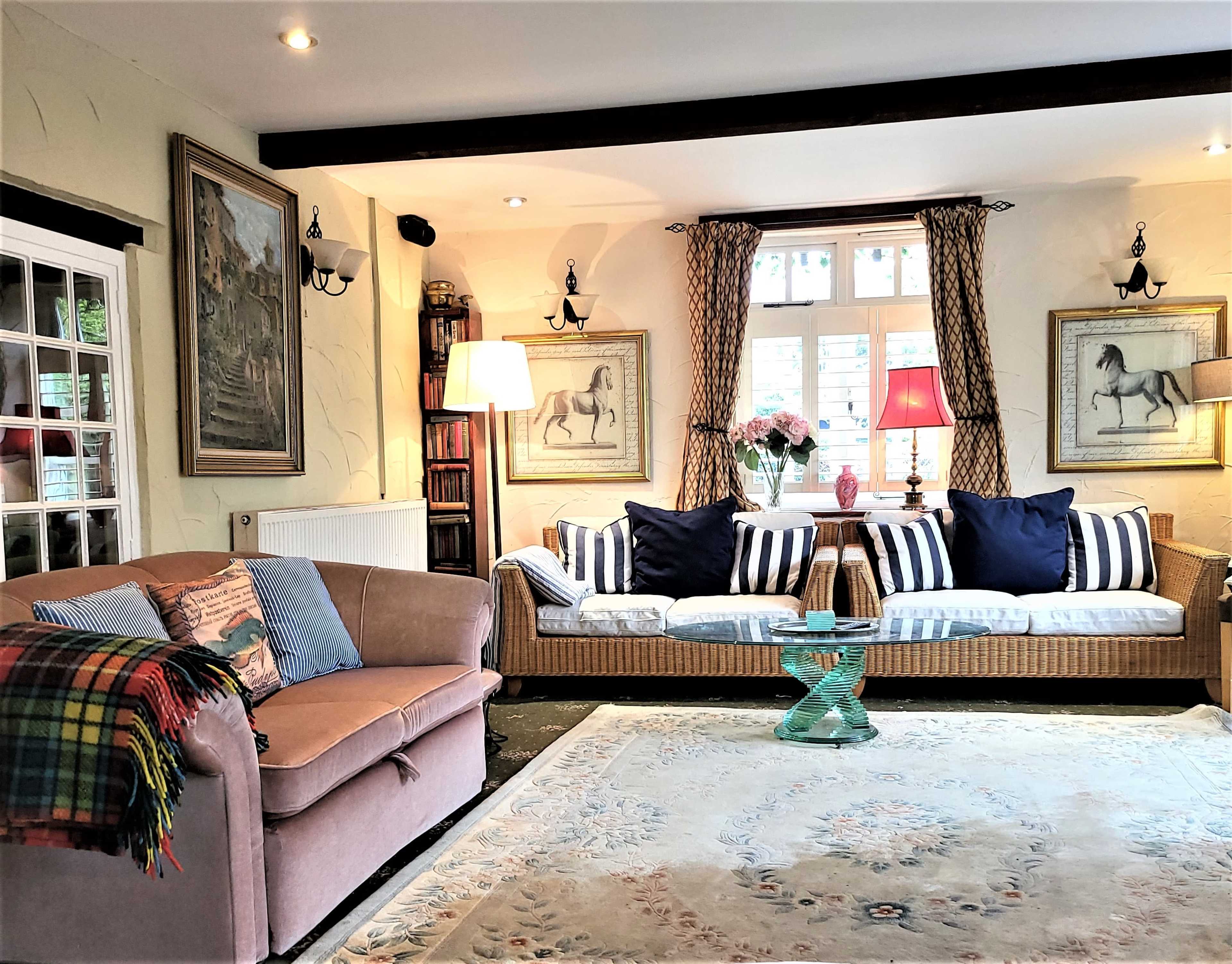 The image shows a cozy living room with two sofas, decorative paintings on the walls, and a patterned rug on the wooden floor.
