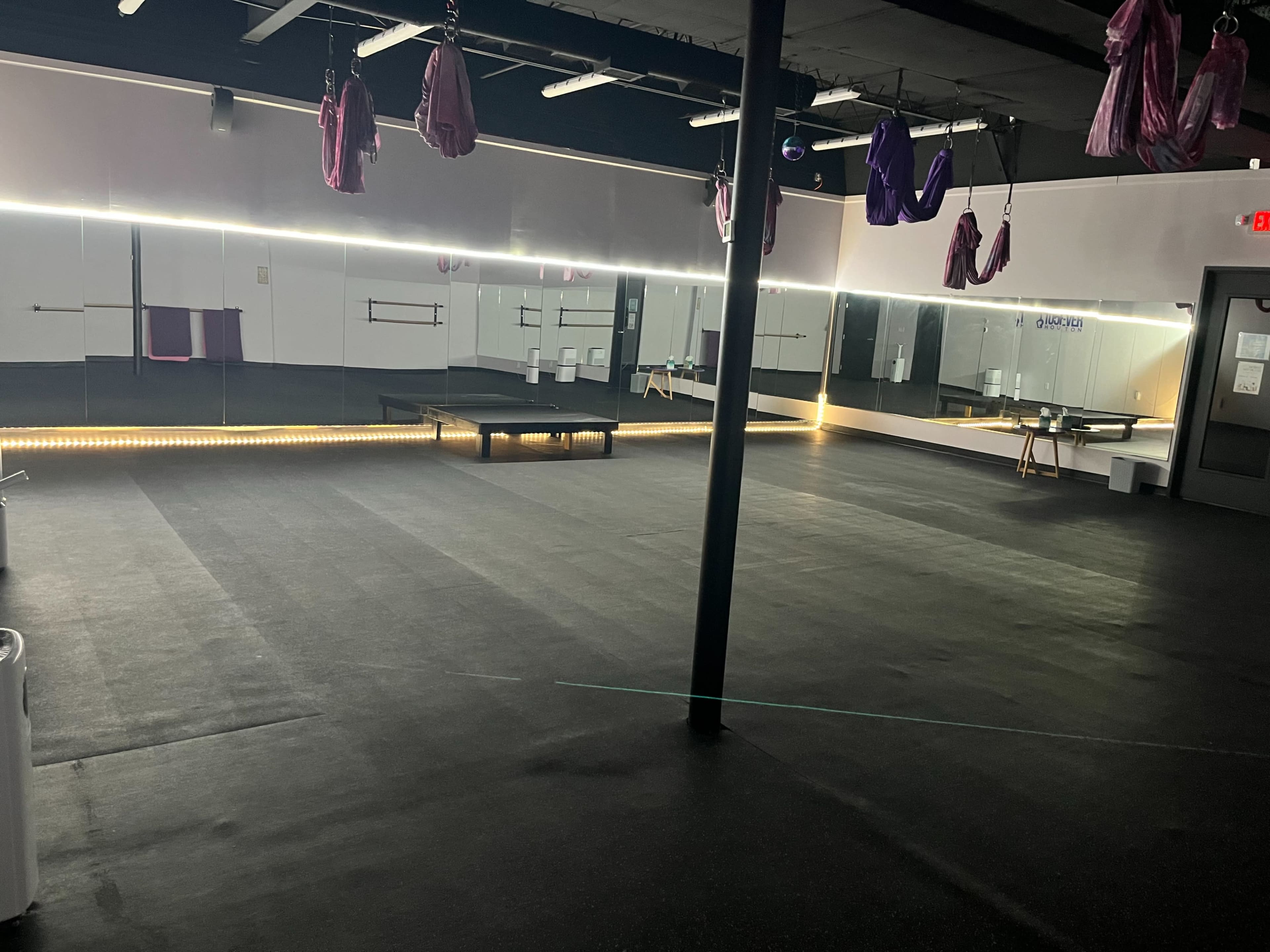 The image shows an empty studio space with dark flooring, mirrored walls, and suspended fabric hammocks for aerial activities.