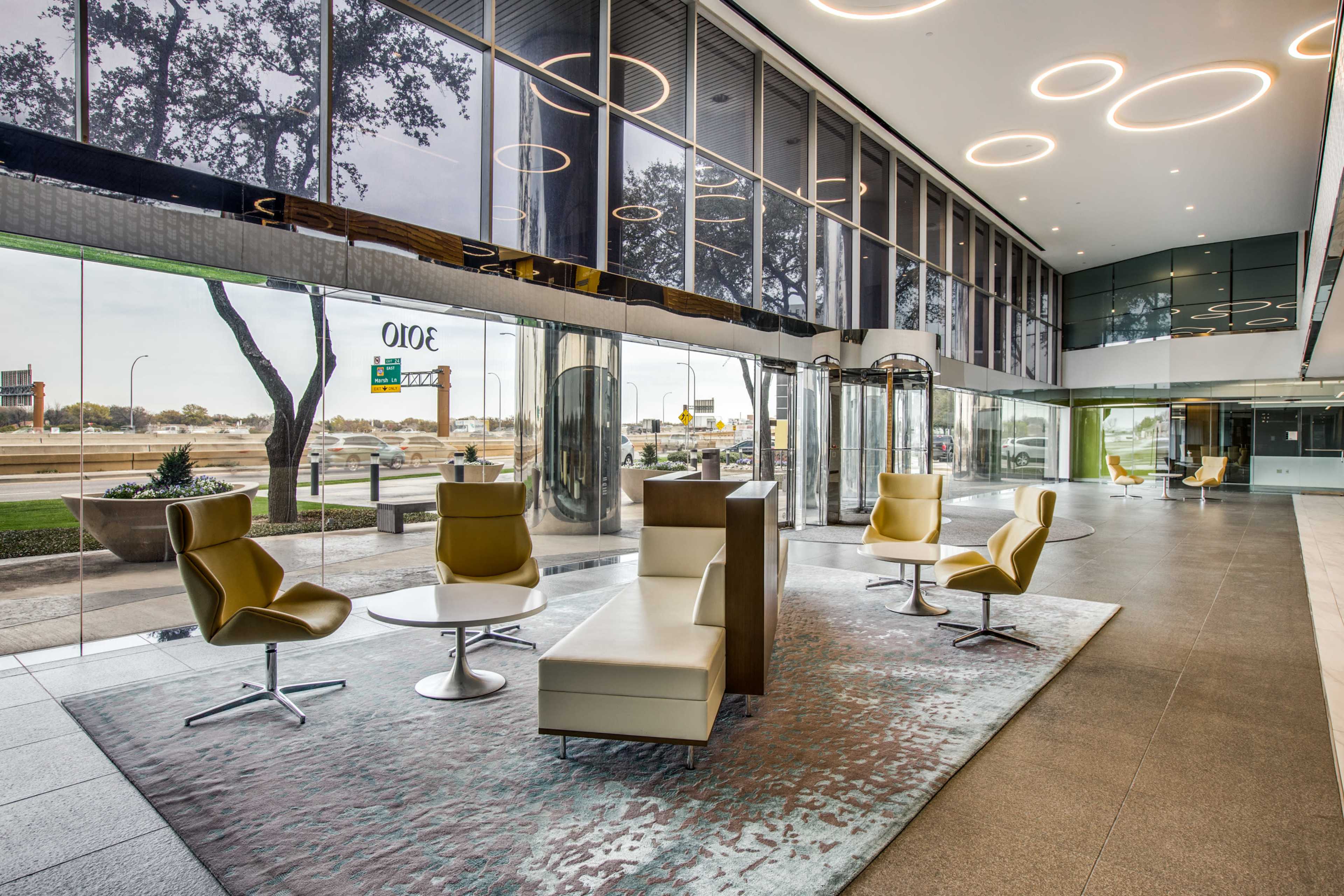 The image shows a modern lobby area featuring sleek furniture, large glass windows, and circular ceiling lights.