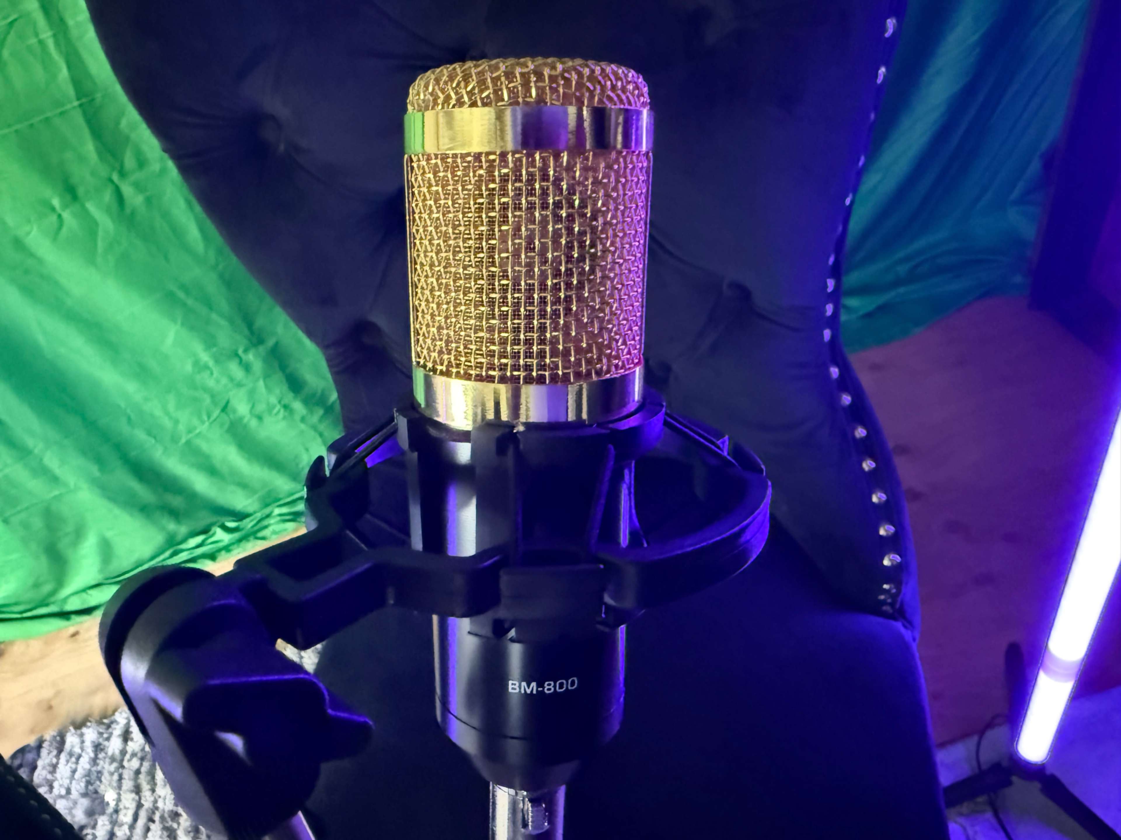 A gold-colored microphone stands on a black mount, positioned in front of a green backdrop.