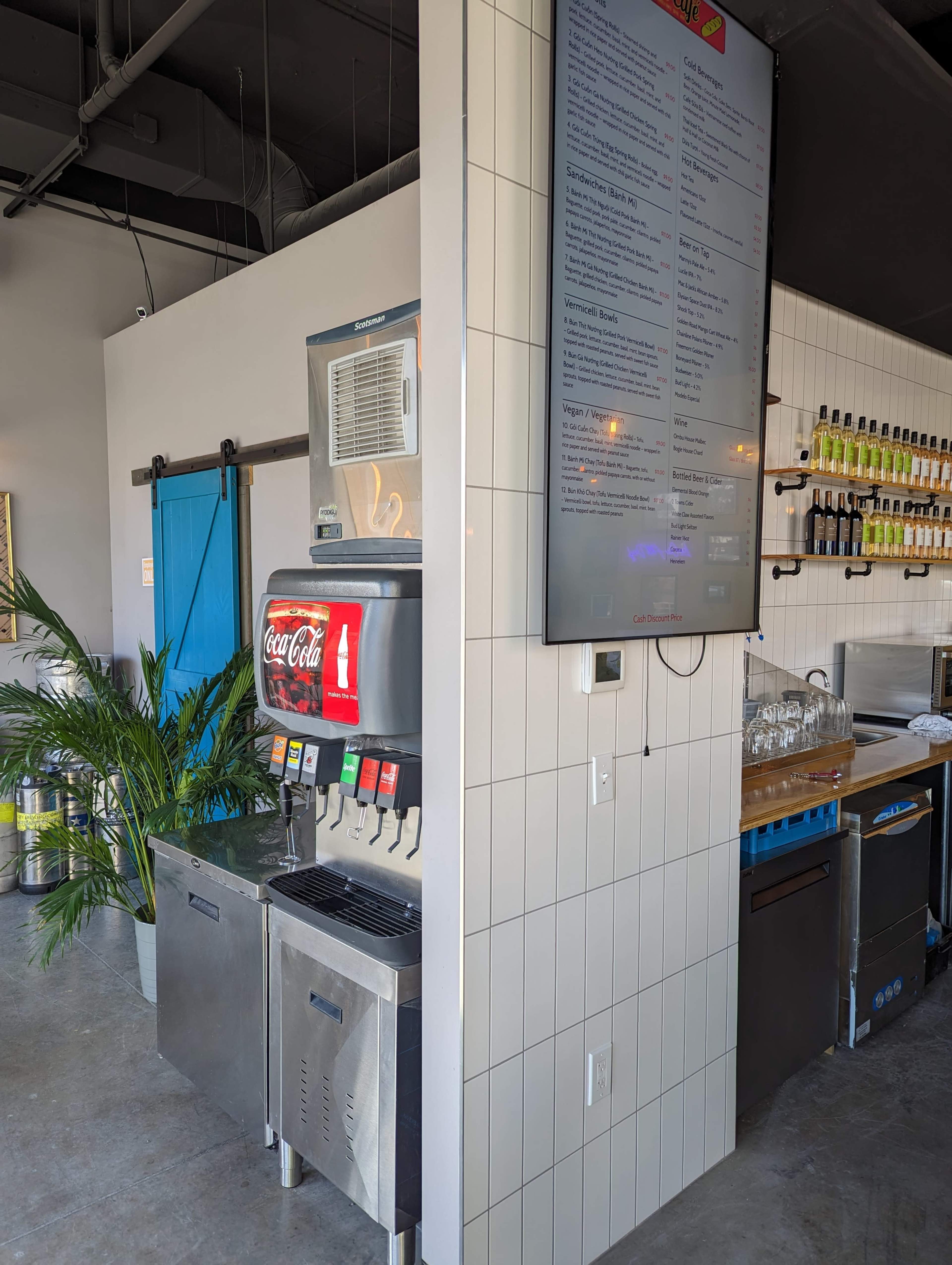 A self-serve Coca-Cola machine positioned next to a digital menu display in a modern café setting.