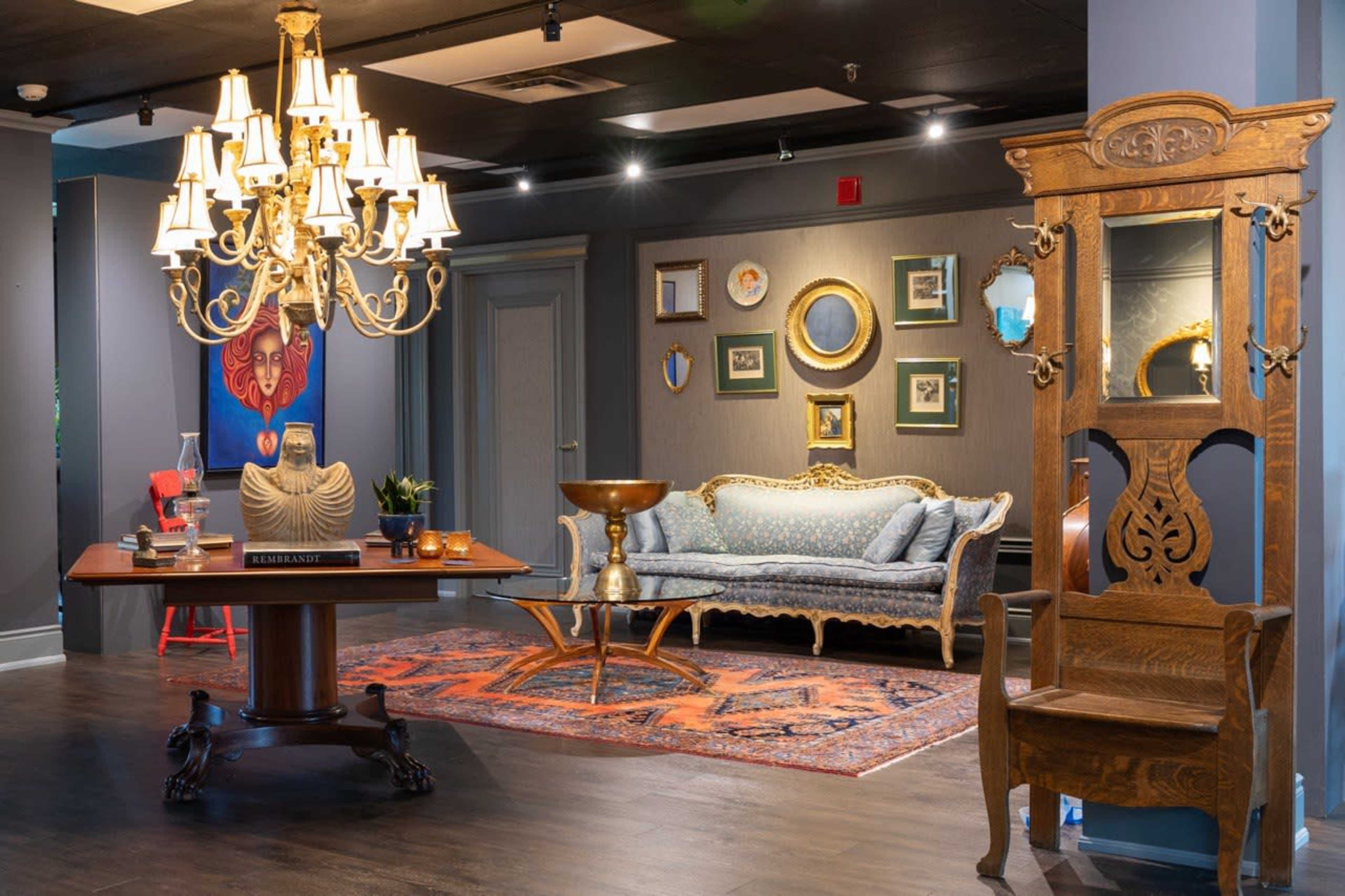 The image features a stylish interior that includes a decorative chandelier, a vintage-looking sofa, an ornate wooden chair, and wall art displayed in an elegant setting.