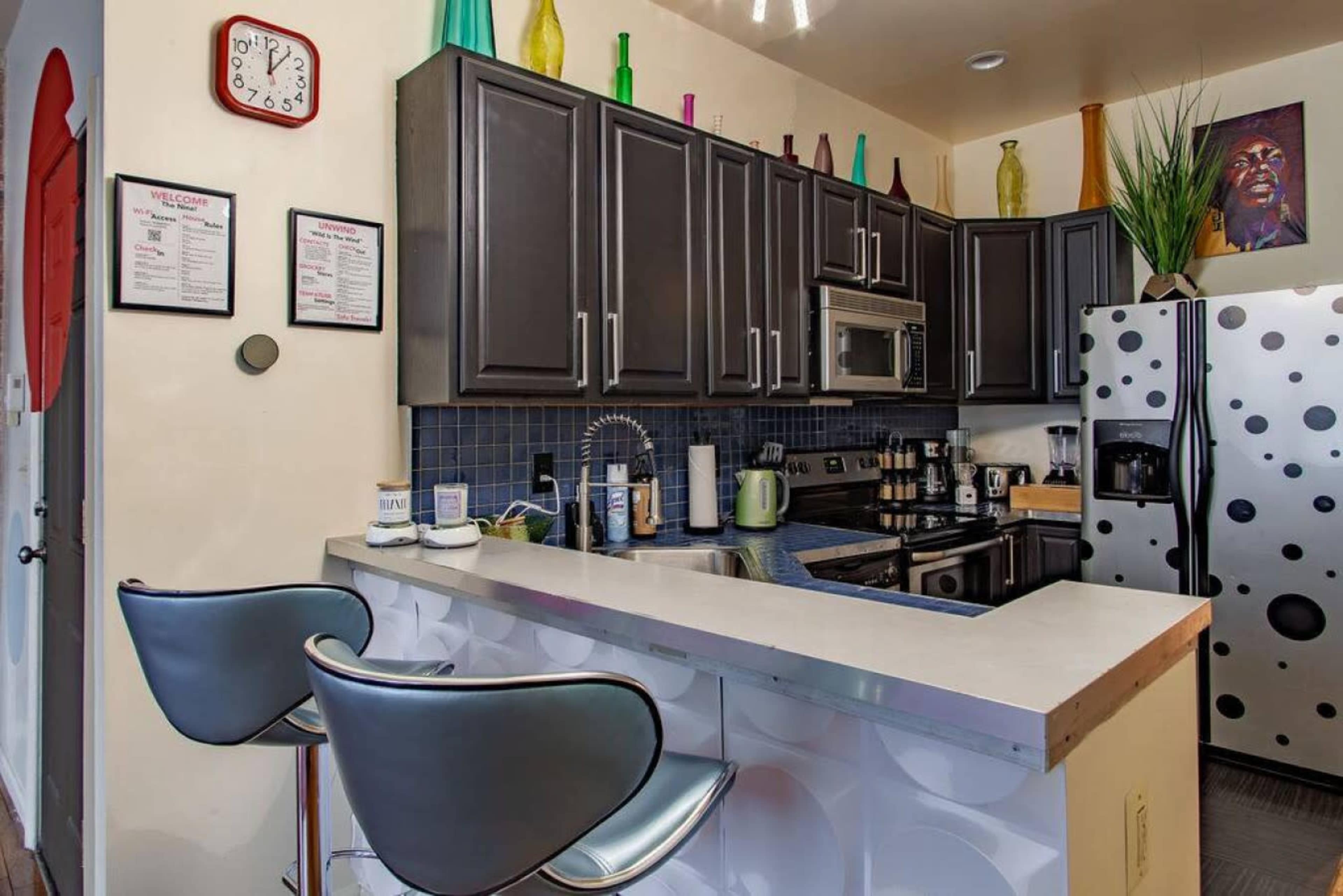 A modern kitchen featuring dark cabinets, a blue tiled backsplash, and a bar area with two sleek stools.
