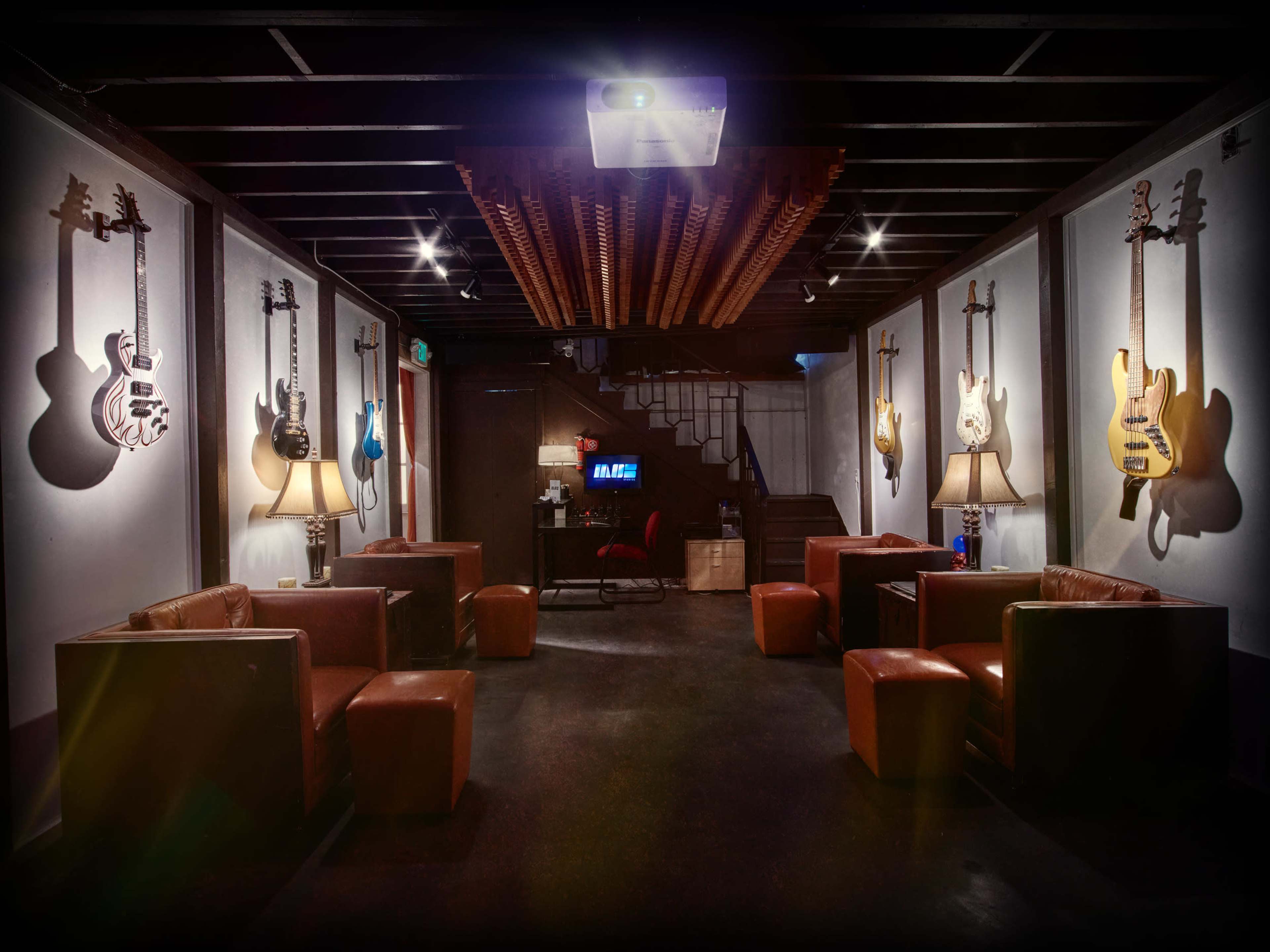 A dimly lit lounge area with brown leather seating and electric guitars hanging on the walls.