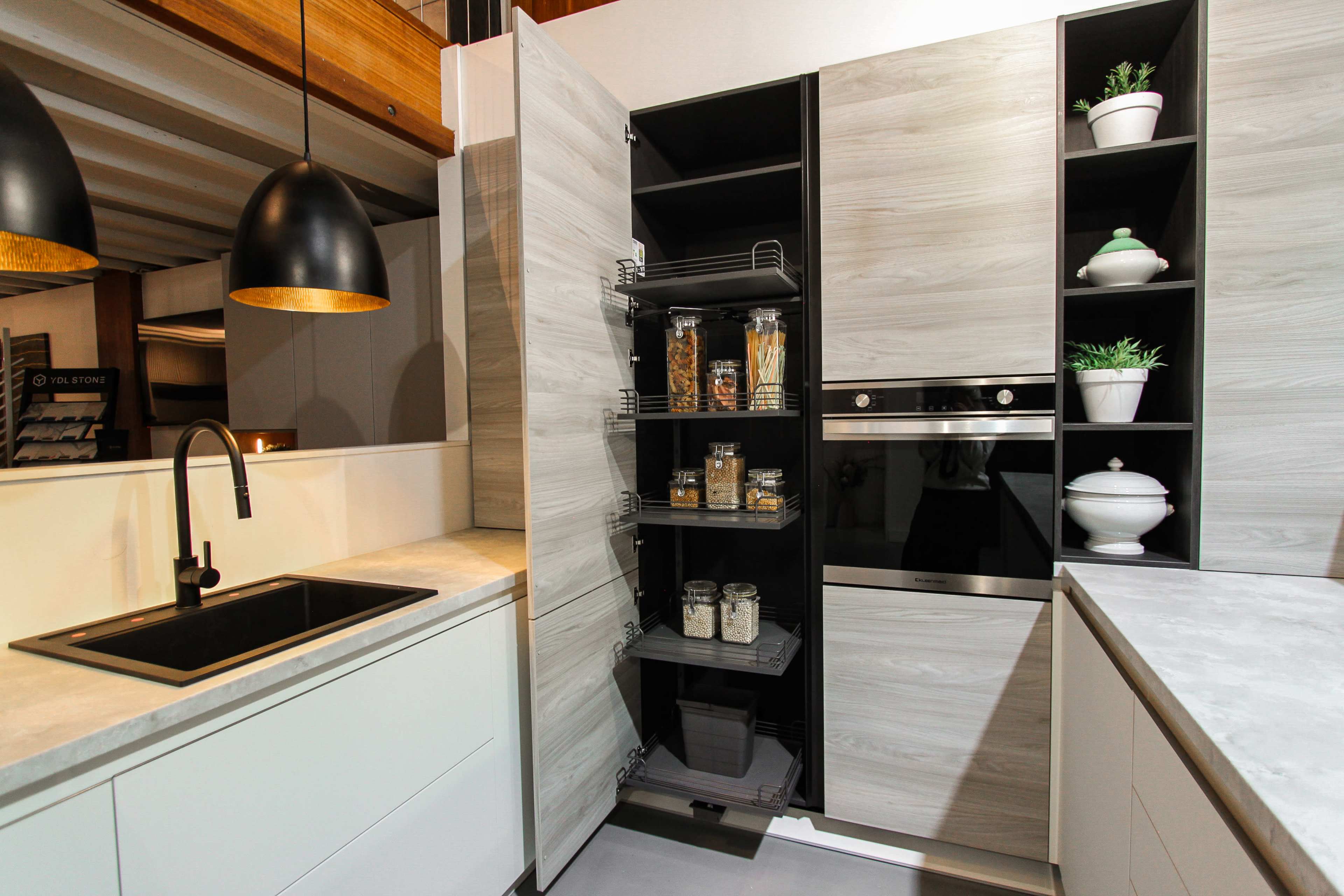 The image shows a modern kitchen featuring a sleek, dual-tone cabinetry with an open pantry revealing neatly arranged jars and containers.