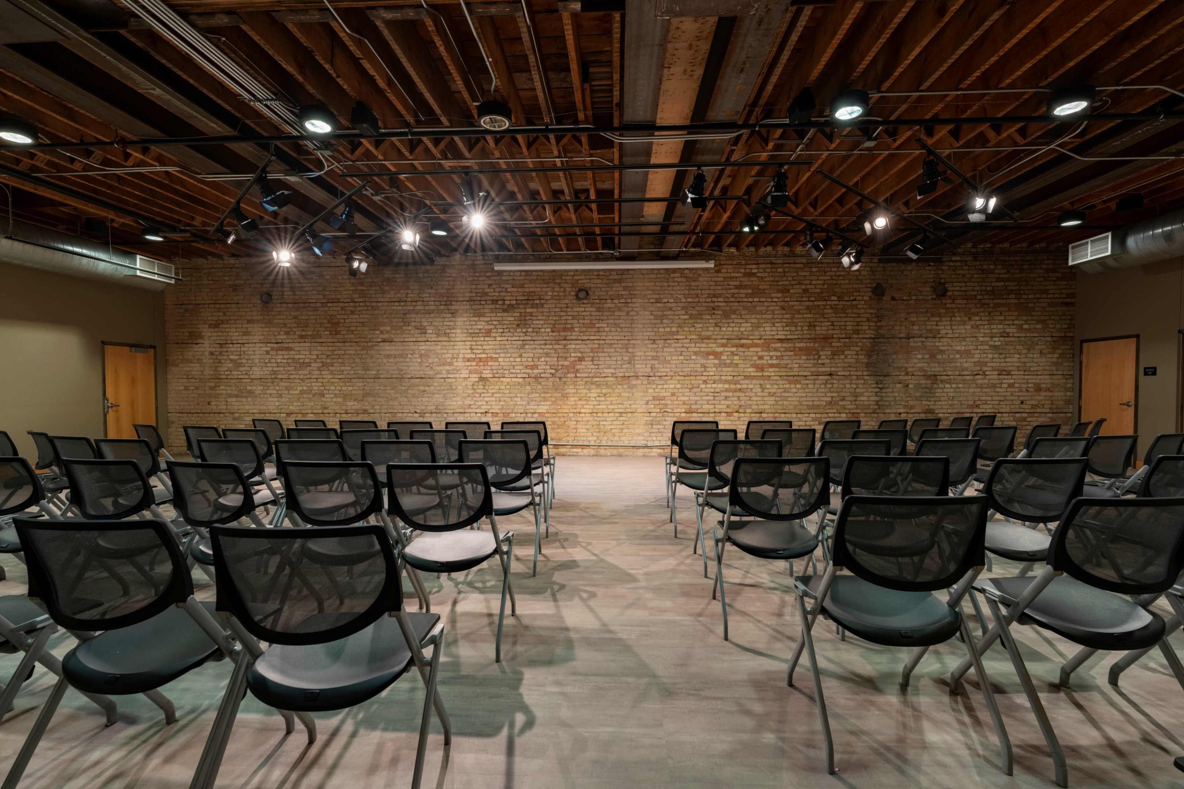 A row of empty black chairs is arranged facing a bare brick wall in a well-lit seminar room.