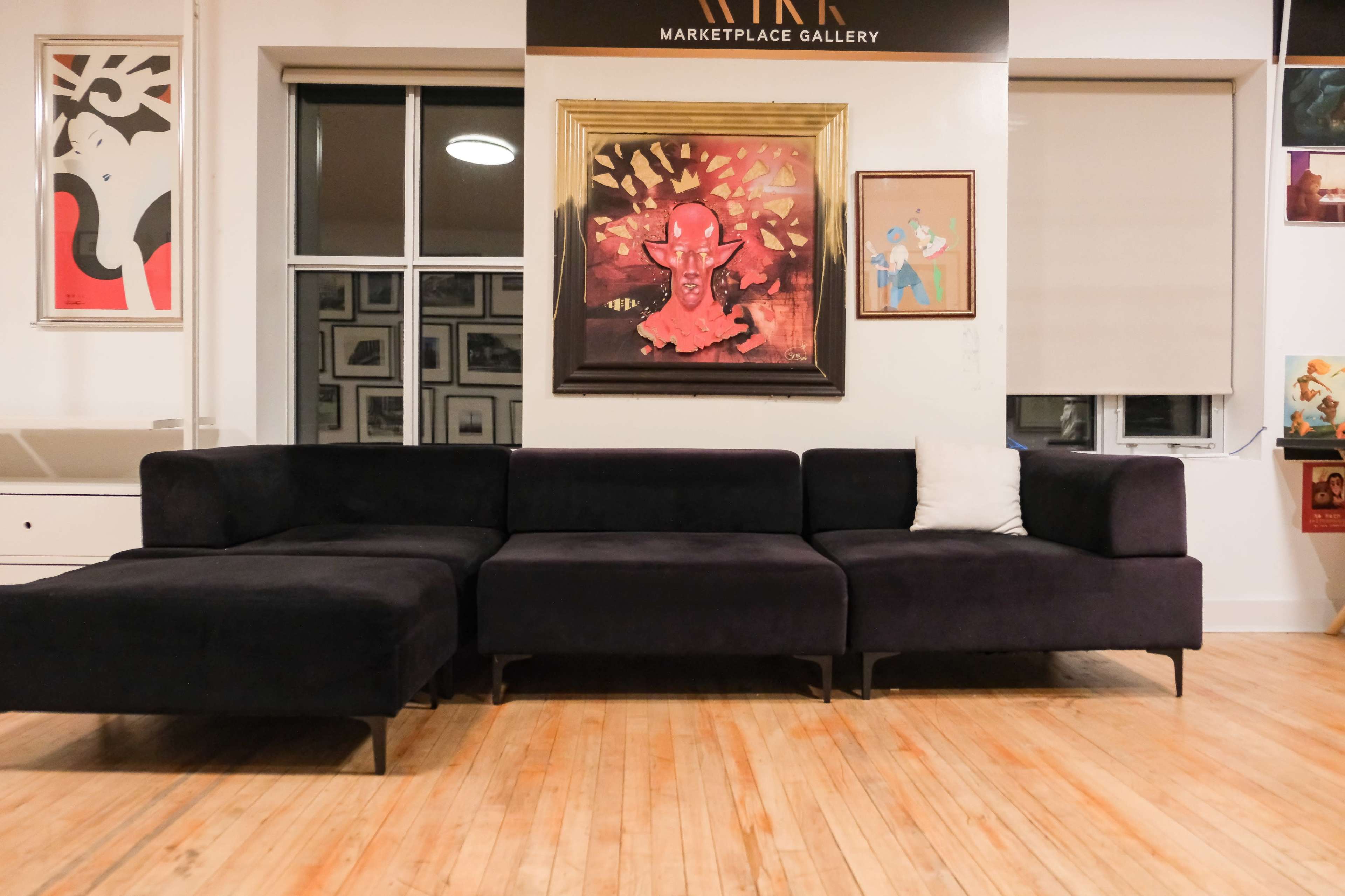 The image shows a modern, dark-colored sectional sofa positioned in a gallery space adorned with various framed artworks on the walls.