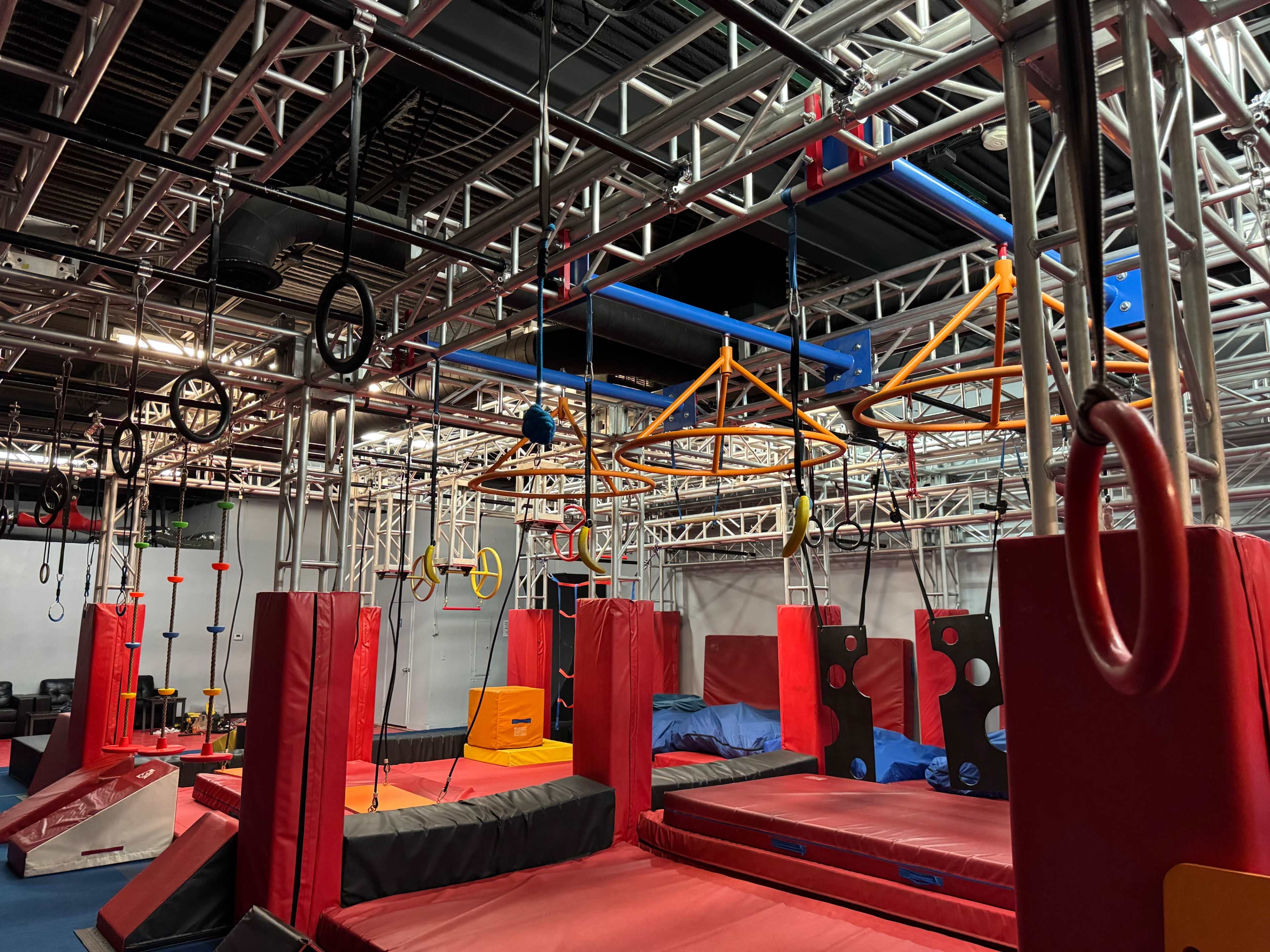 The image shows an indoor obstacle course with various apparatuses, including ropes, rings, and padded structures for physical activities.