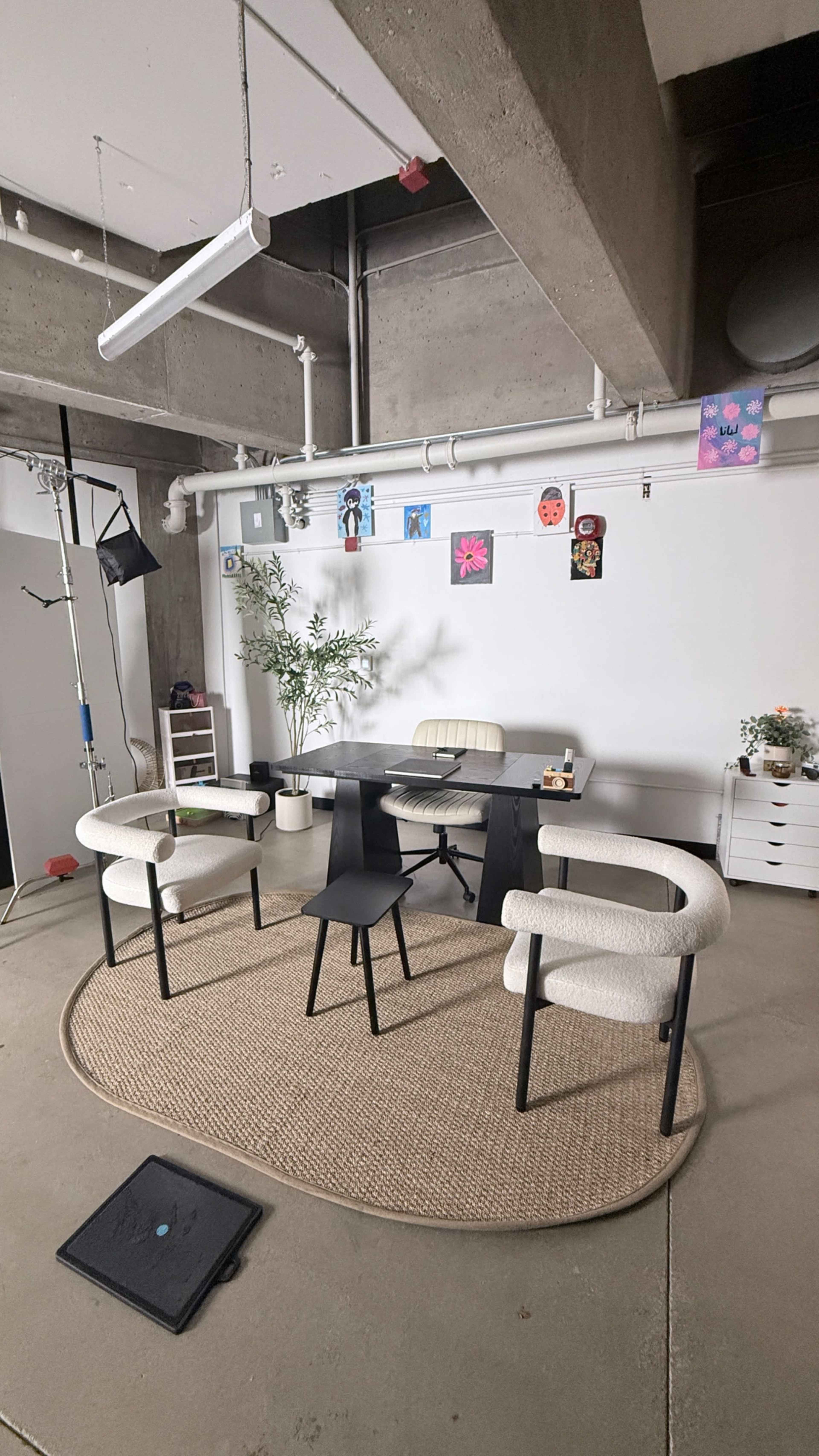 The image shows a modern office space with a round rug, a desk surrounded by three chairs, and colorful artwork displayed on the walls.