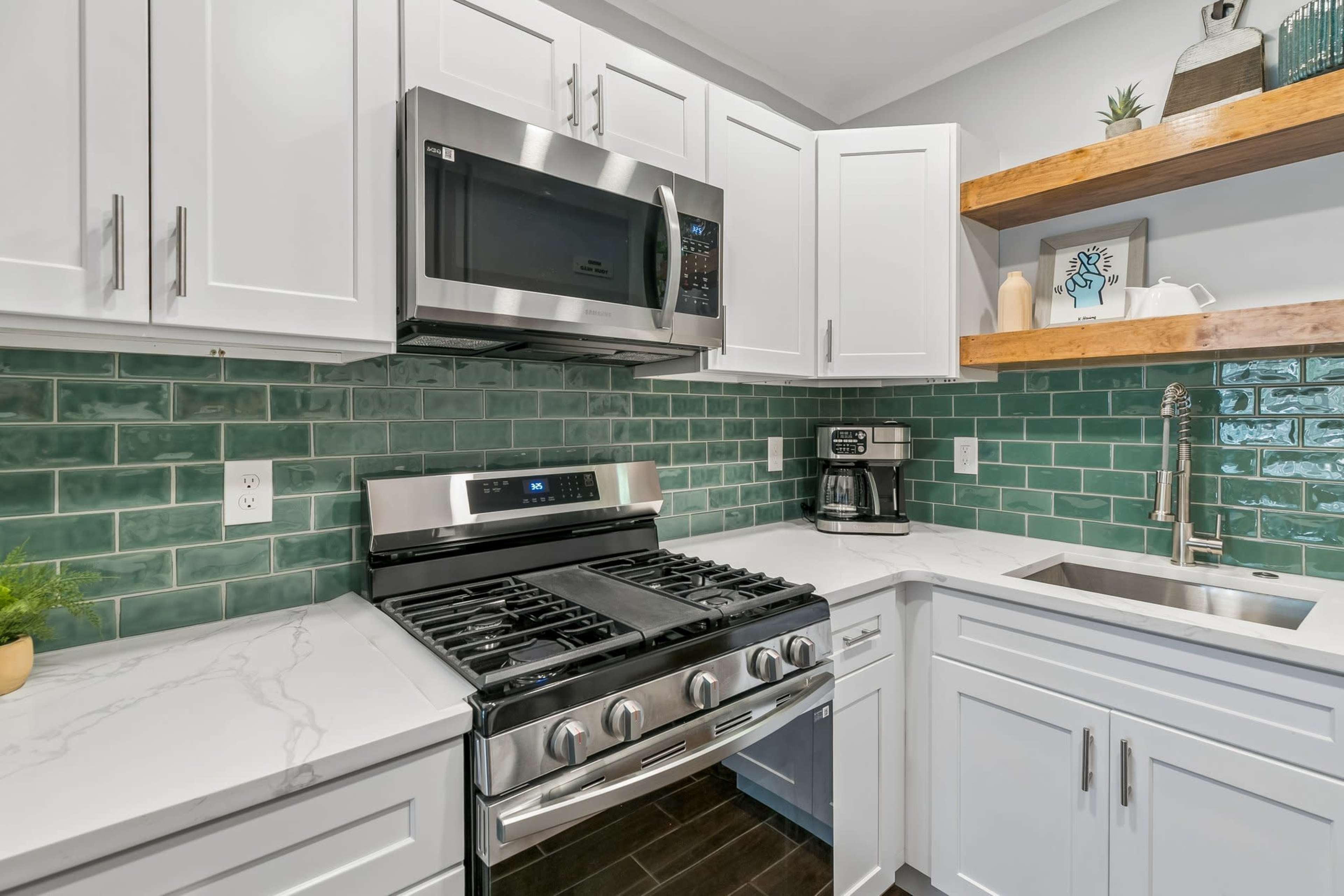 The image shows a modern kitchen with white cabinetry, a stainless steel microwave and oven, green subway tile backsplash, and a marble countertop.