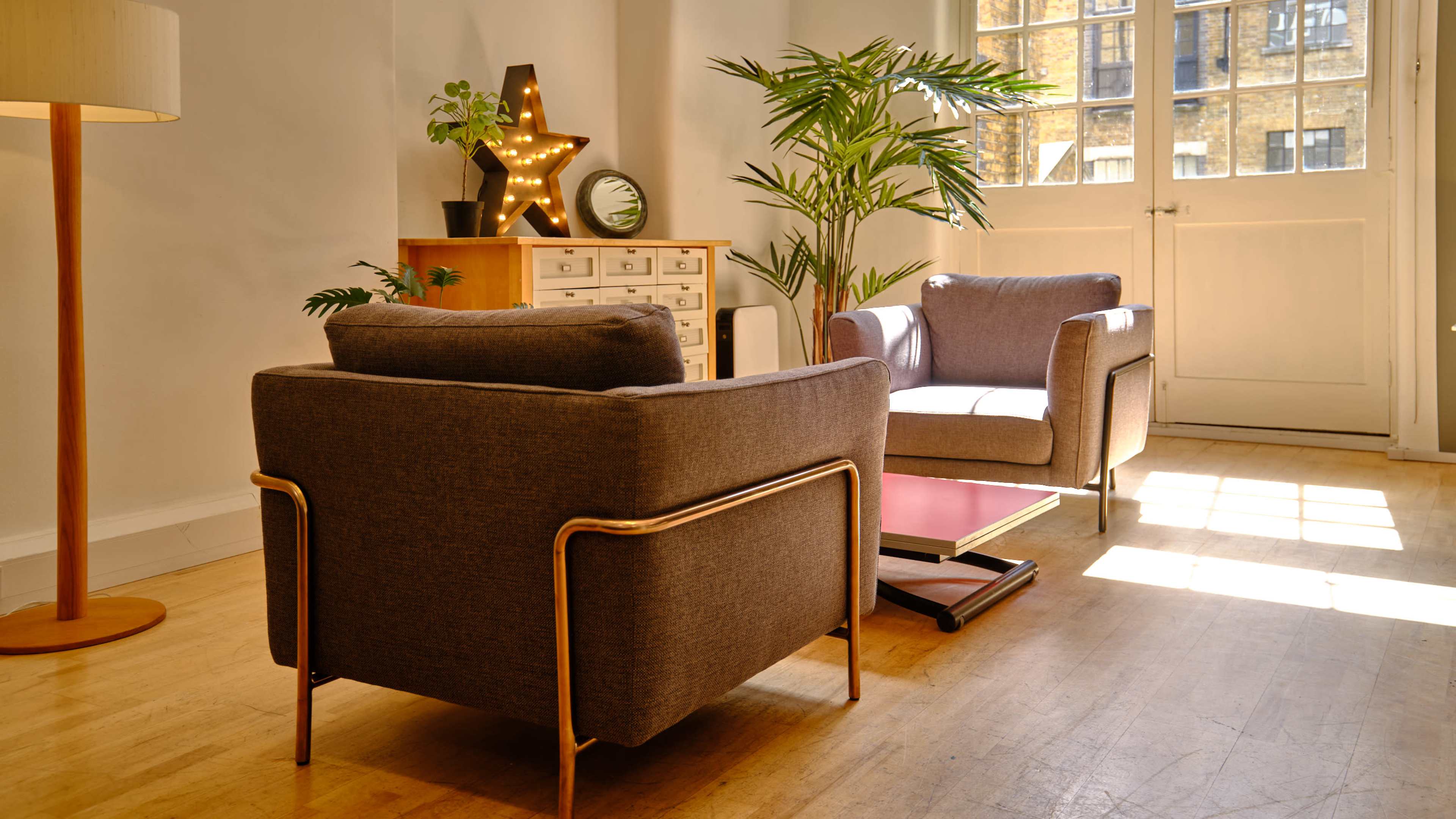 The scene features a cozy living area with two gray armchairs facing each other, a star-shaped light decoration, a potted plant, and a wooden storage unit near a large window.