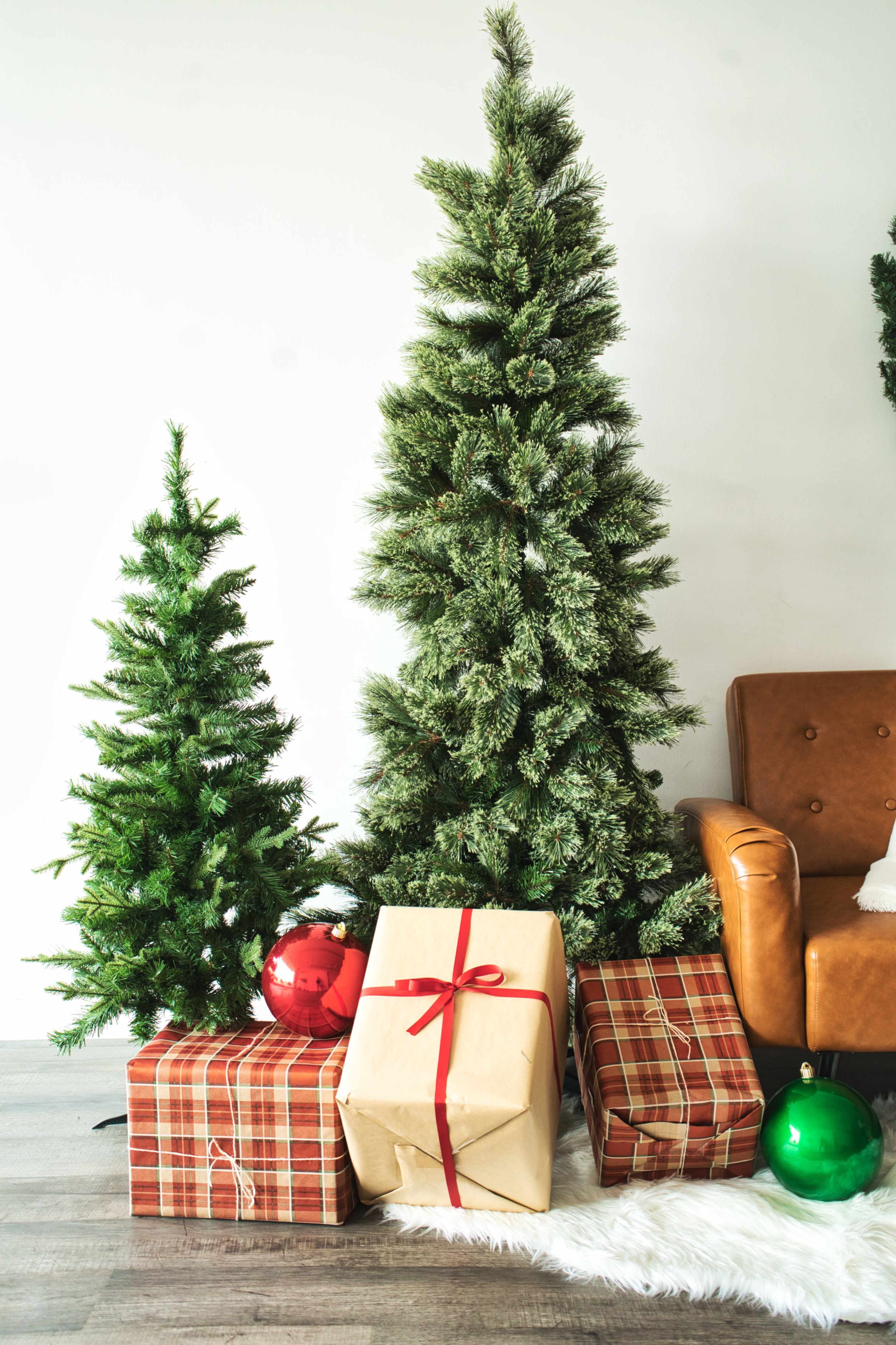 The scene features two Christmas trees beside a brown leather chair, with wrapped presents and ornaments arranged neatly on the floor.