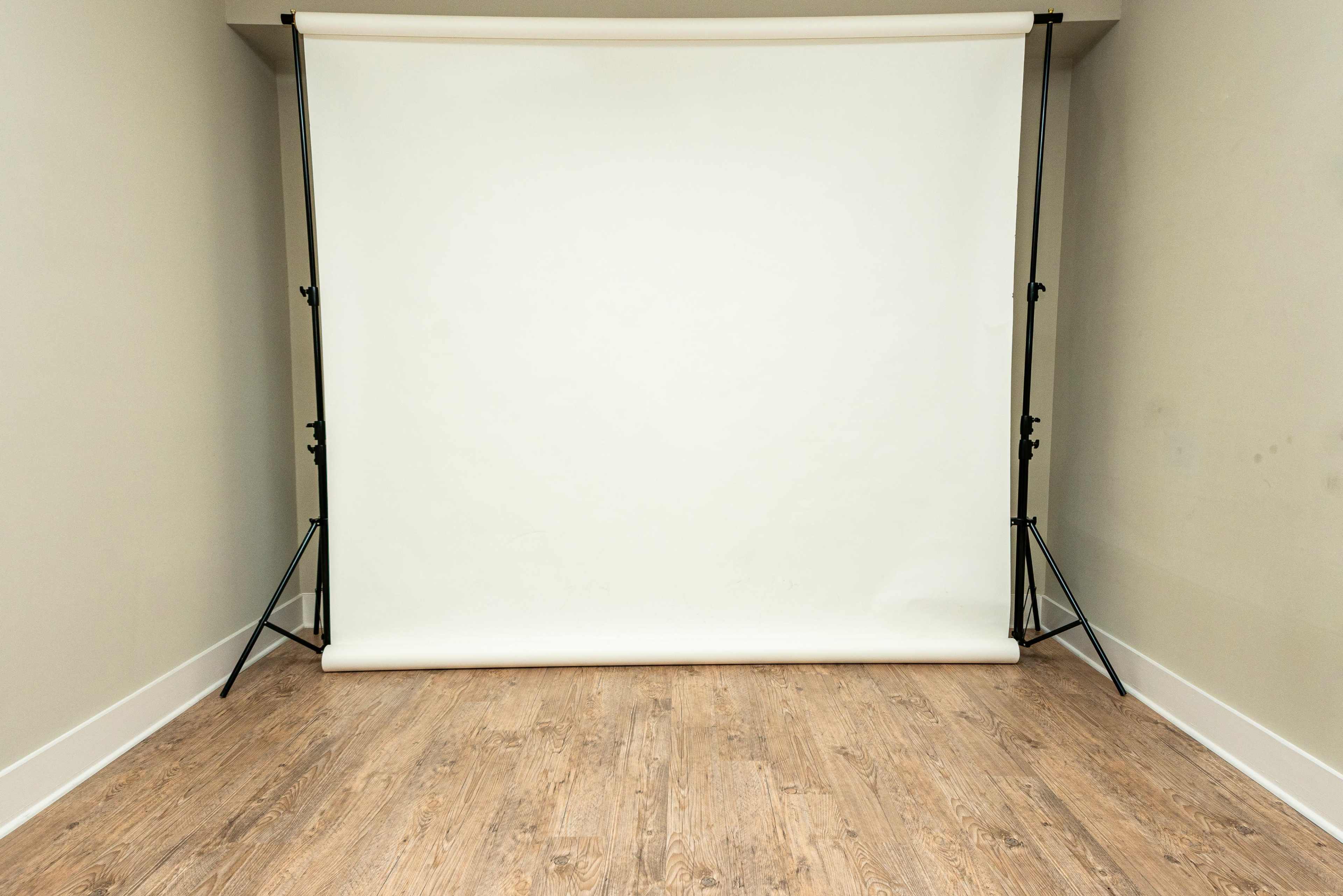A blank photography backdrop is set up in a room with wooden flooring.