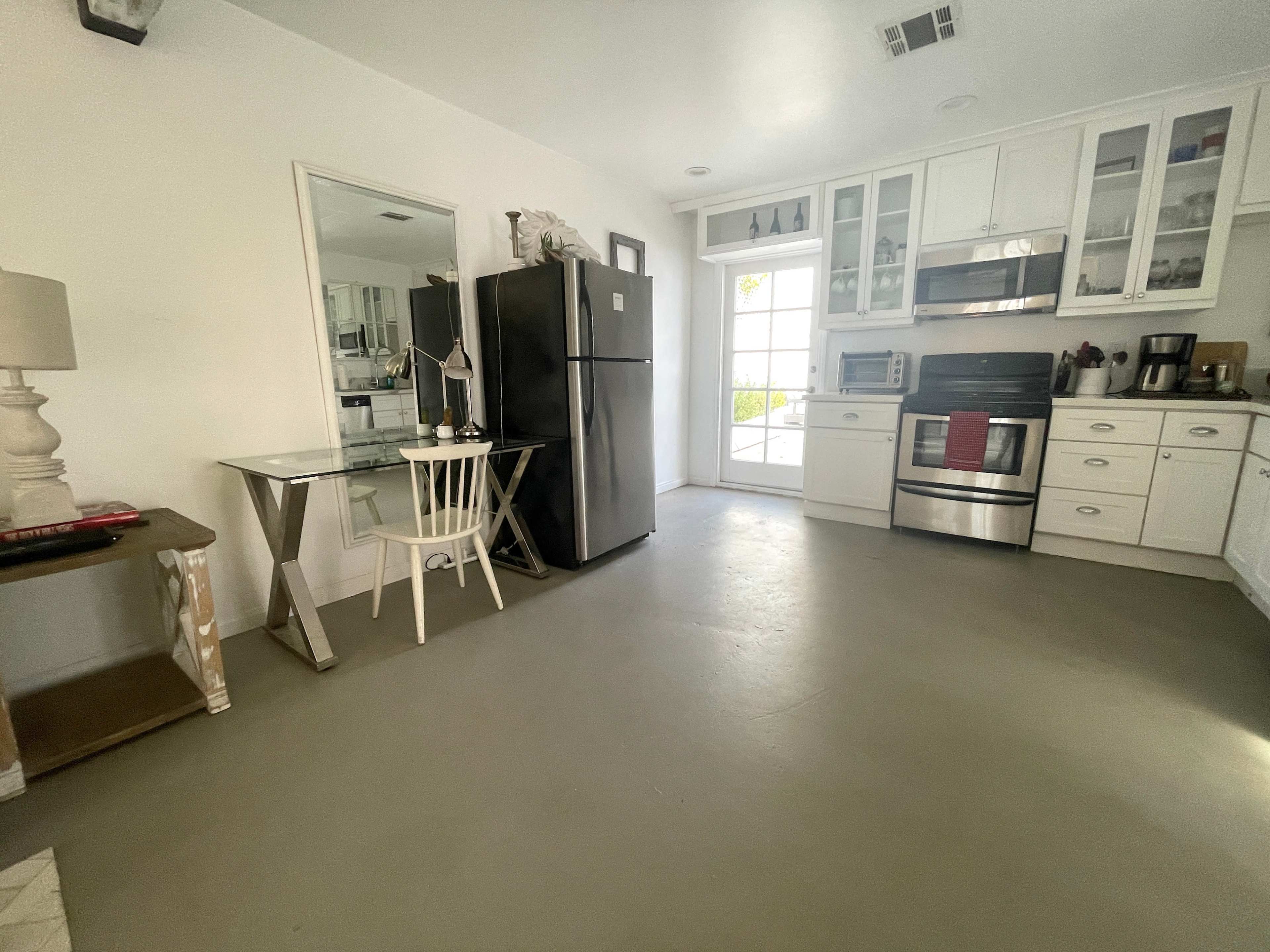 The image shows a modern kitchen with a refrigerator, stove, and a small dining table set against a light-colored floor.