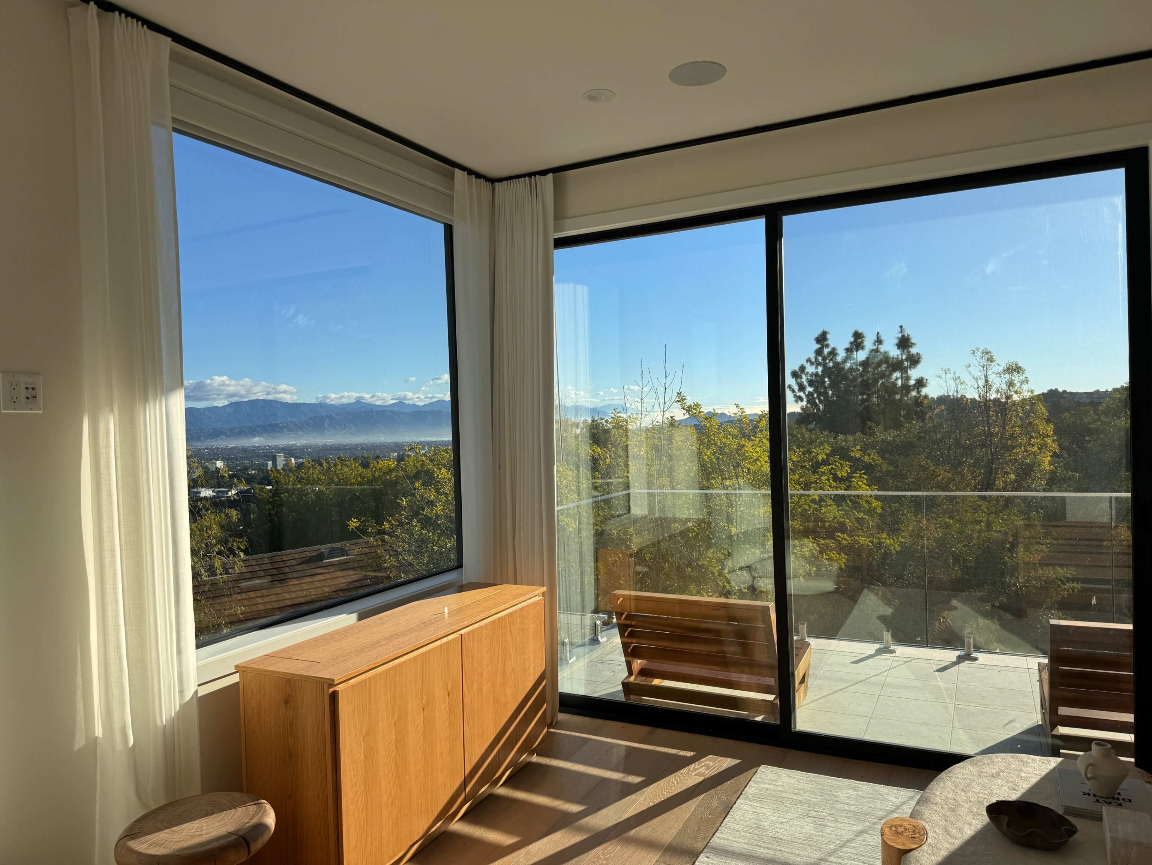 A modern living room features large windows that offer a view of a mountainous landscape under a clear sky.