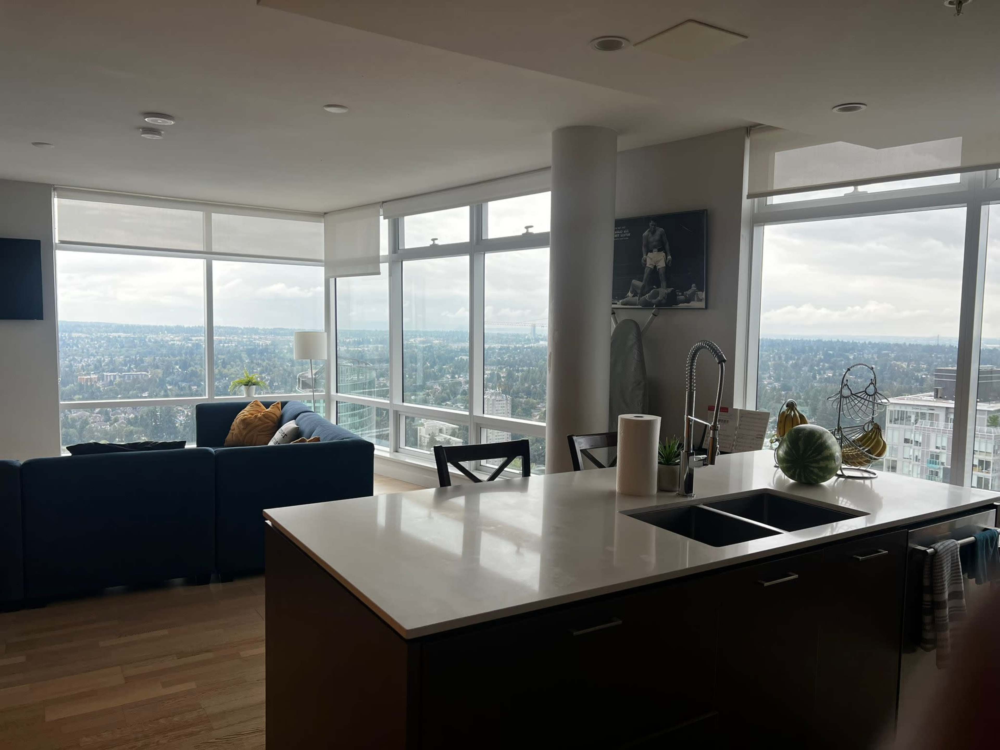 A modern kitchen with a large island overlooks a city skyline through expansive windows in a high-rise apartment.