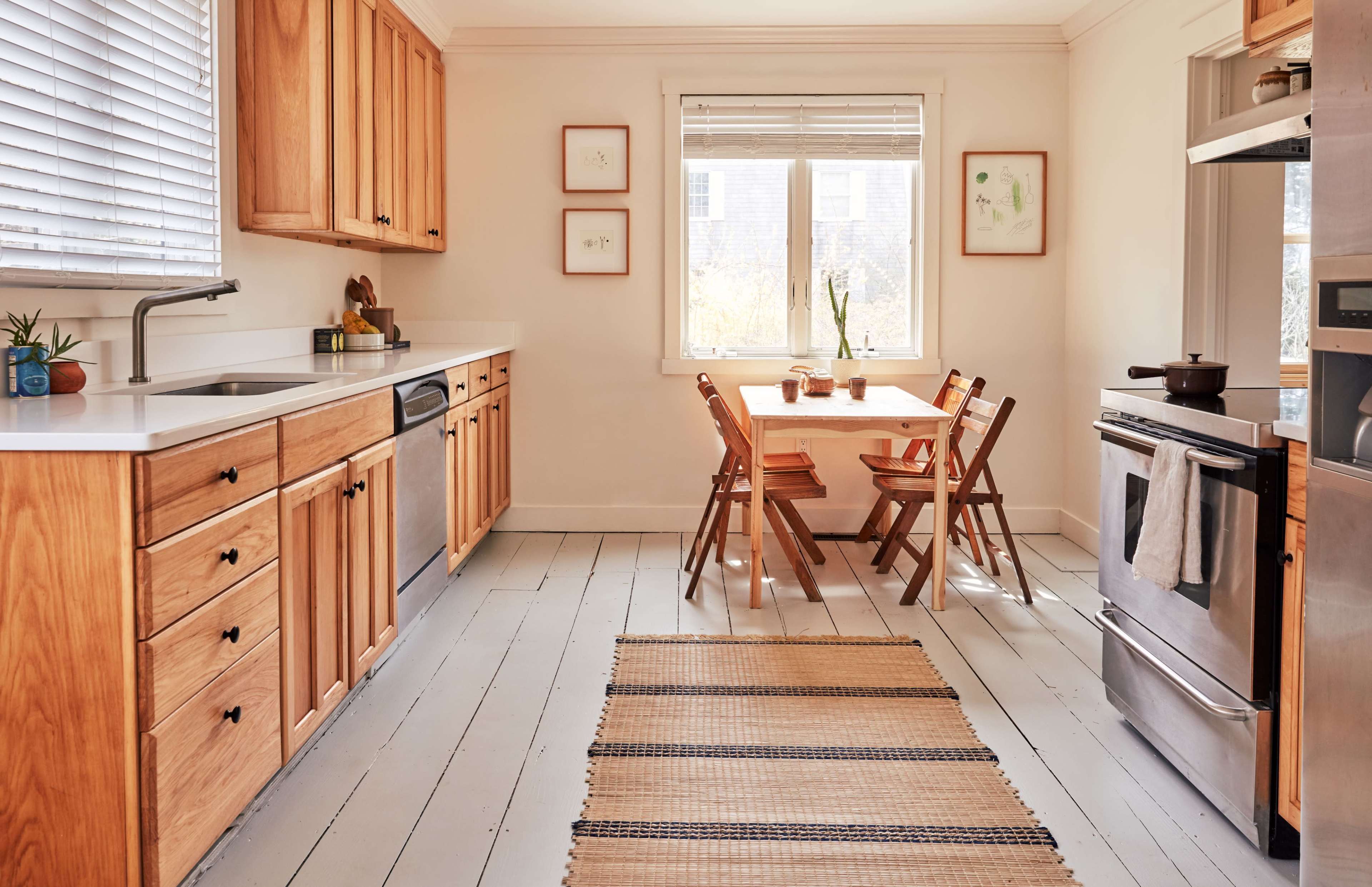 A modern kitchen features wooden cabinets, a stainless steel dishwasher, a dining table with chairs, and a window overlooking the outdoors.