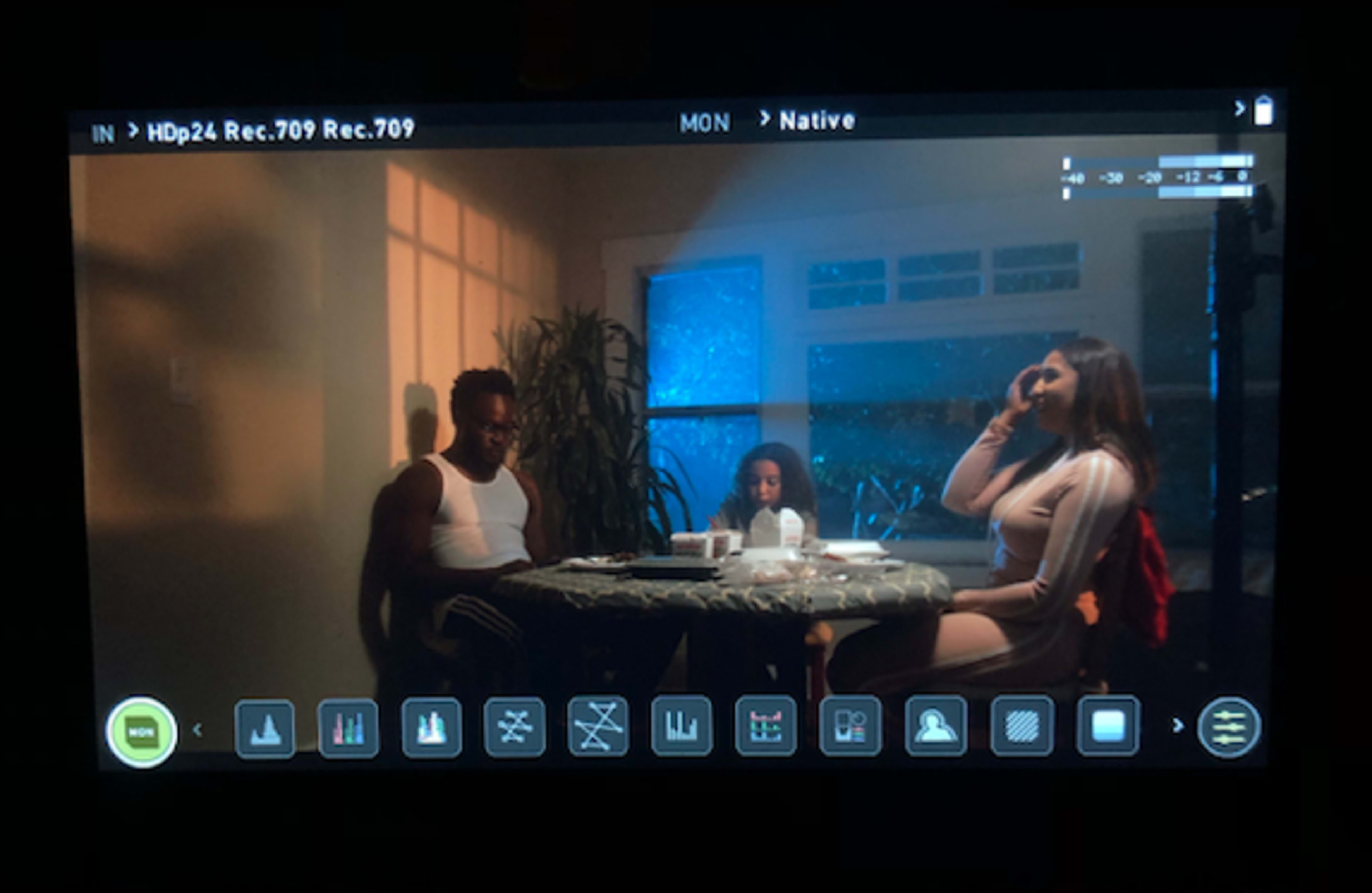 Three people sitting around a table in a dimly lit room, with a window revealing rain outside.