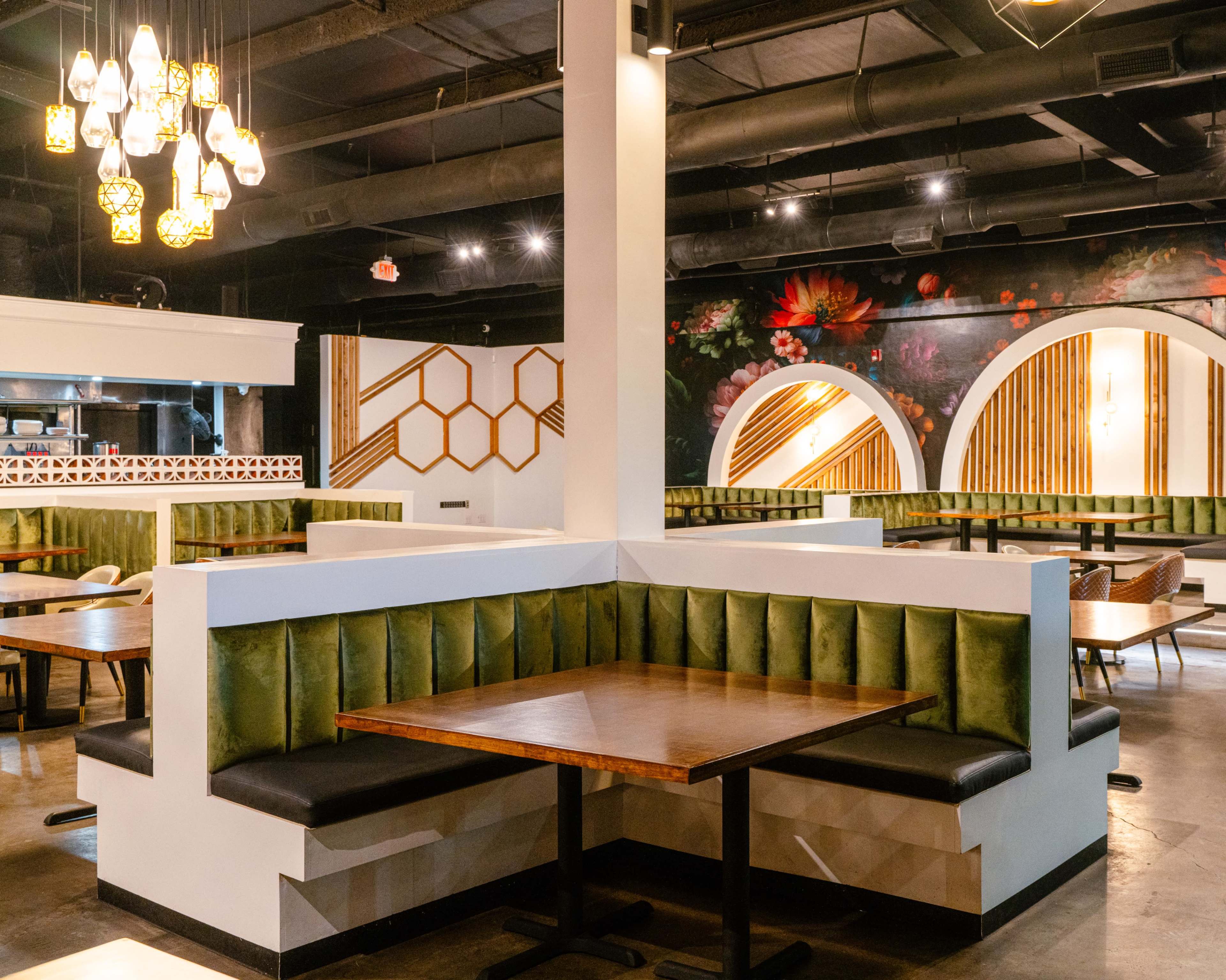 The image shows a modern restaurant interior with green upholstered seating, wooden tables, and decorative wall art featuring floral elements.
