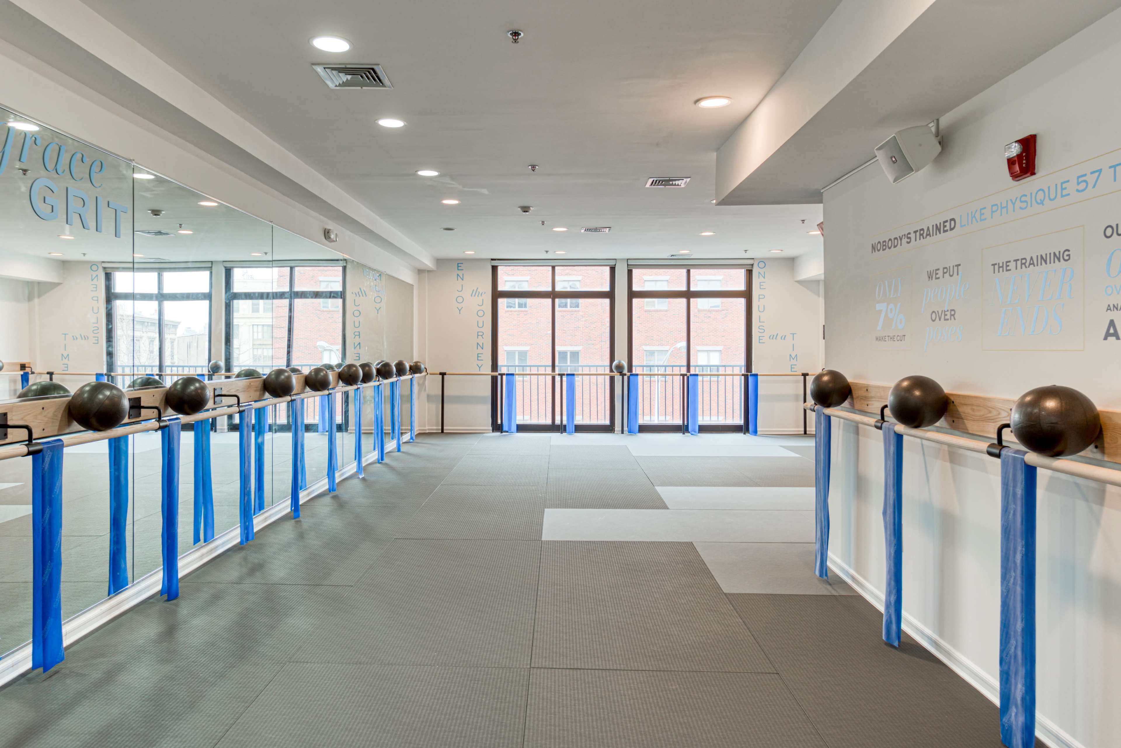 The image shows a spacious fitness studio with large mirrors, exercise equipment, and a light-colored flooring design.