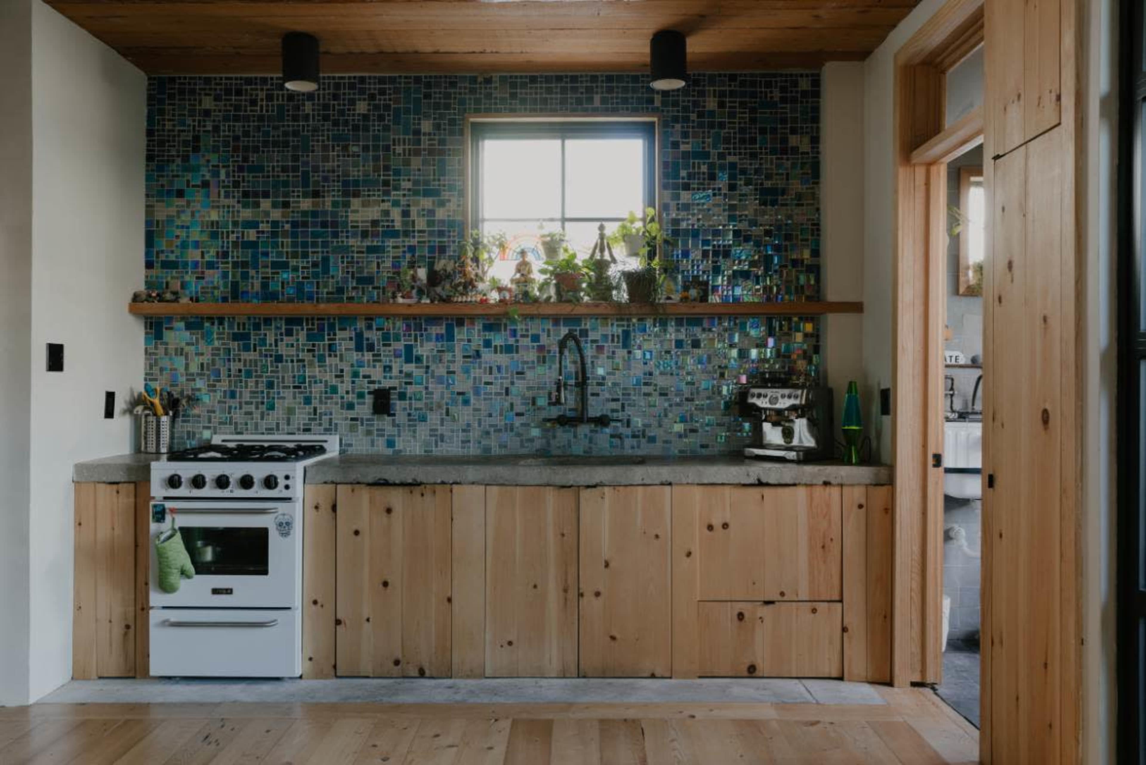 A kitchen featuring a blue mosaic tile backsplash, a wooden countertop, a white stove, and a window above the sink.