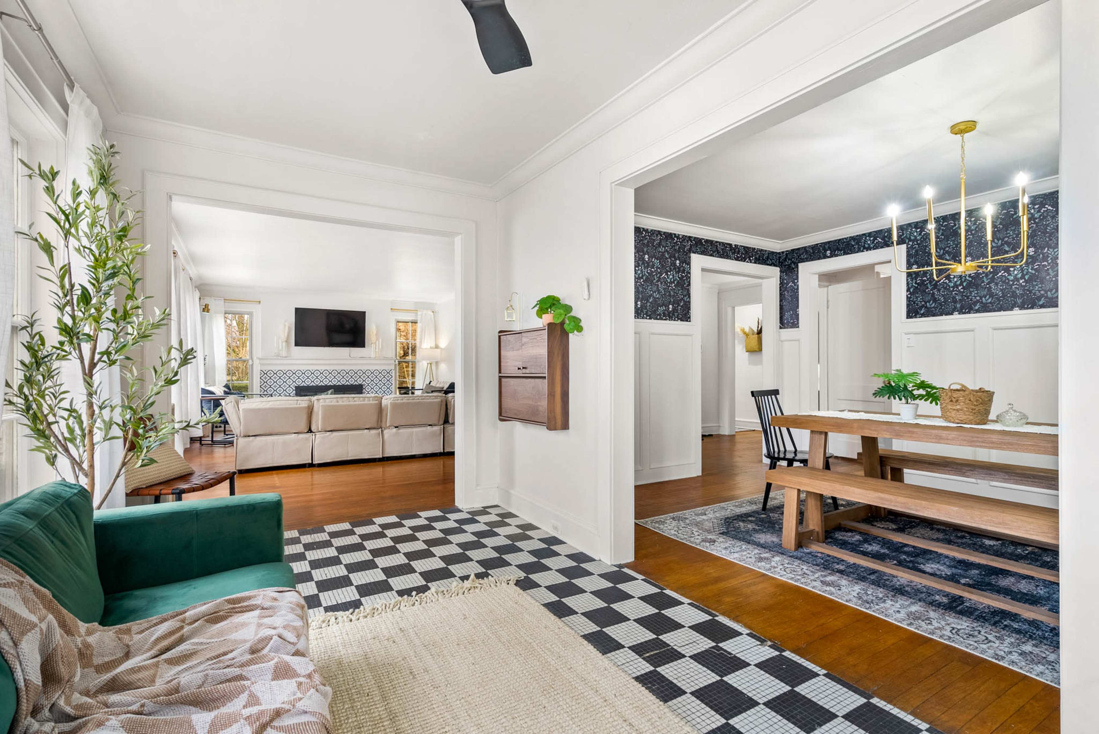 A foyer leading to an open living area, featuring a dining table and a cozy seating arrangement with a checkered floor and decorative elements.