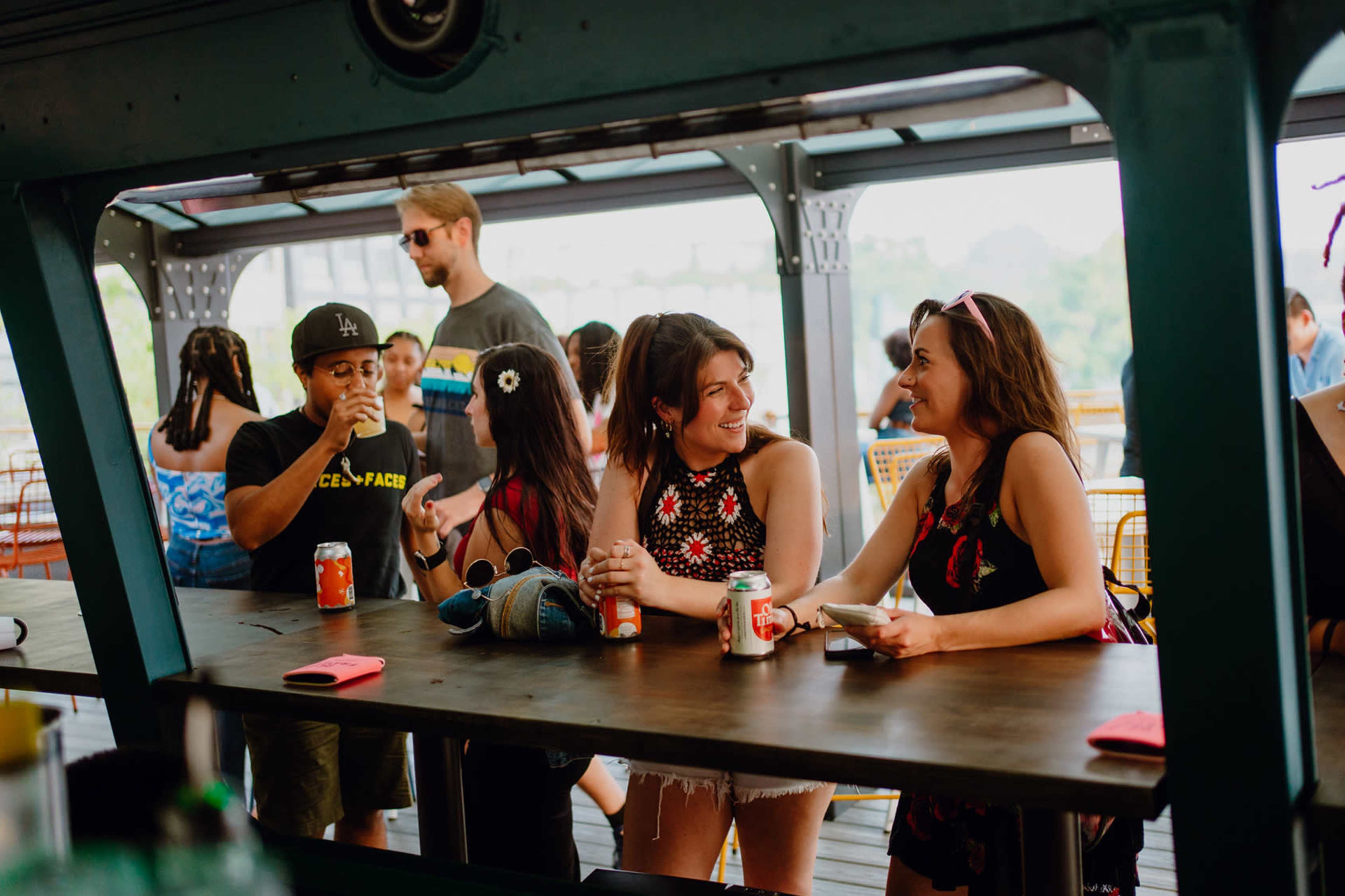 A group of people socializes at a bar on an outdoor deck, enjoying drinks and engaging in conversation.
