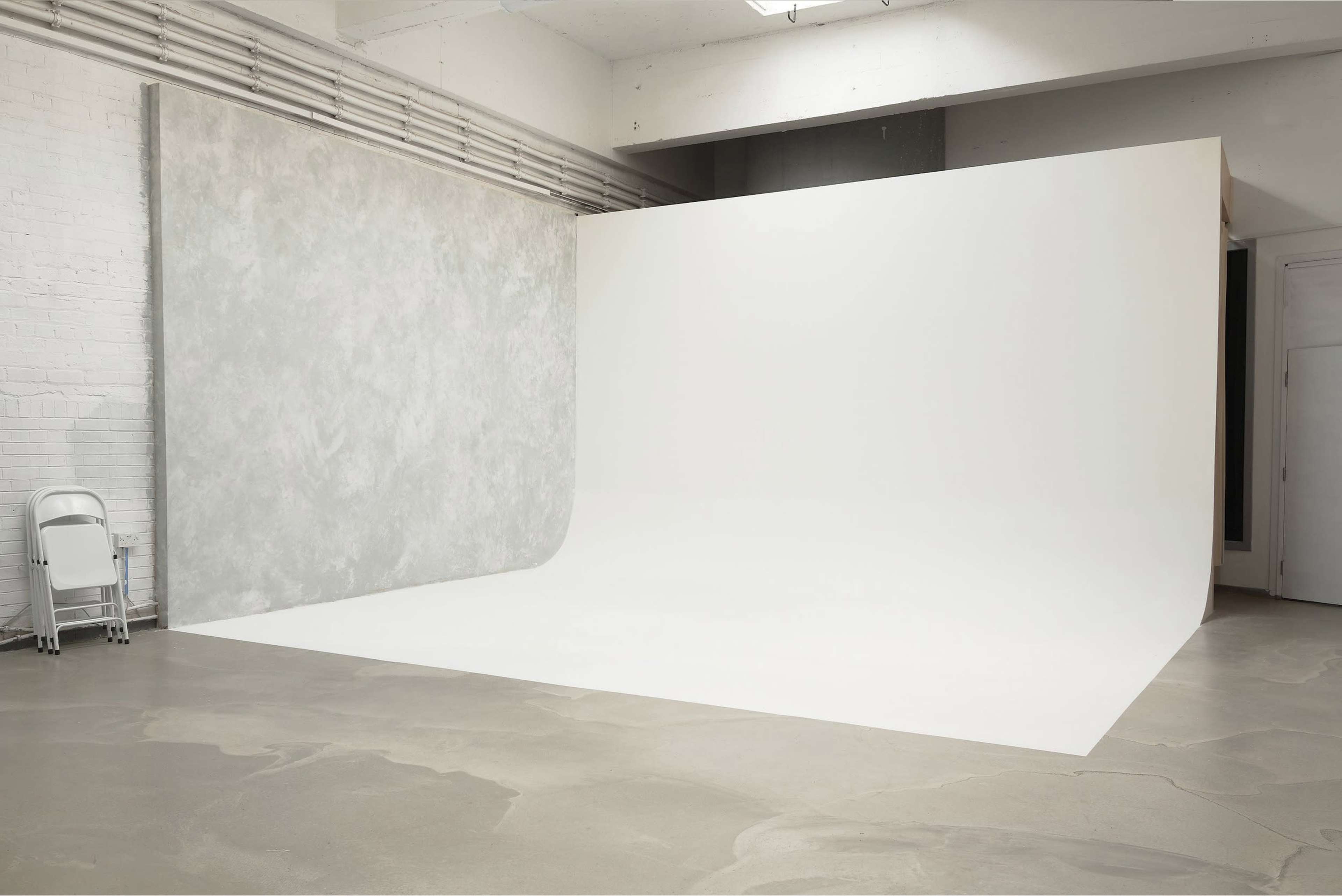 A spacious photo studio with a seamless white backdrop and a textured gray wall.