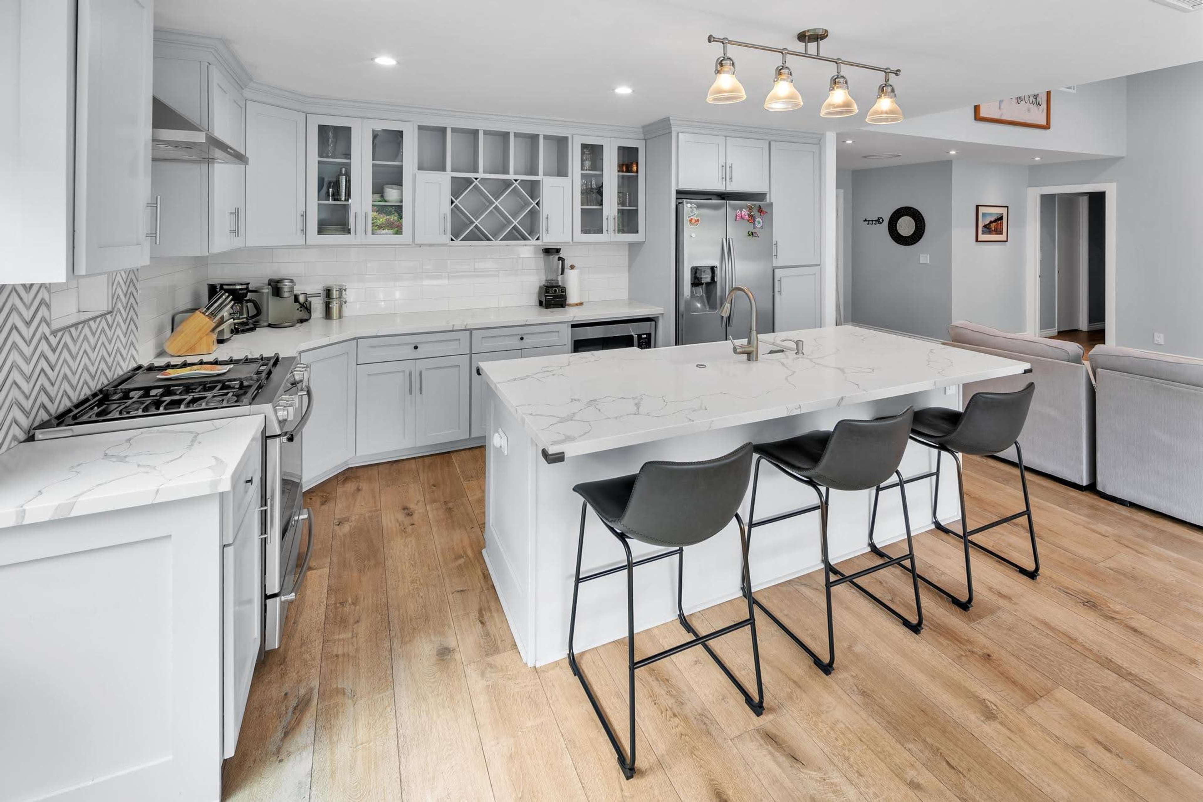 A modern kitchen features light blue cabinetry, a large island with seating for four, and stainless steel appliances.
