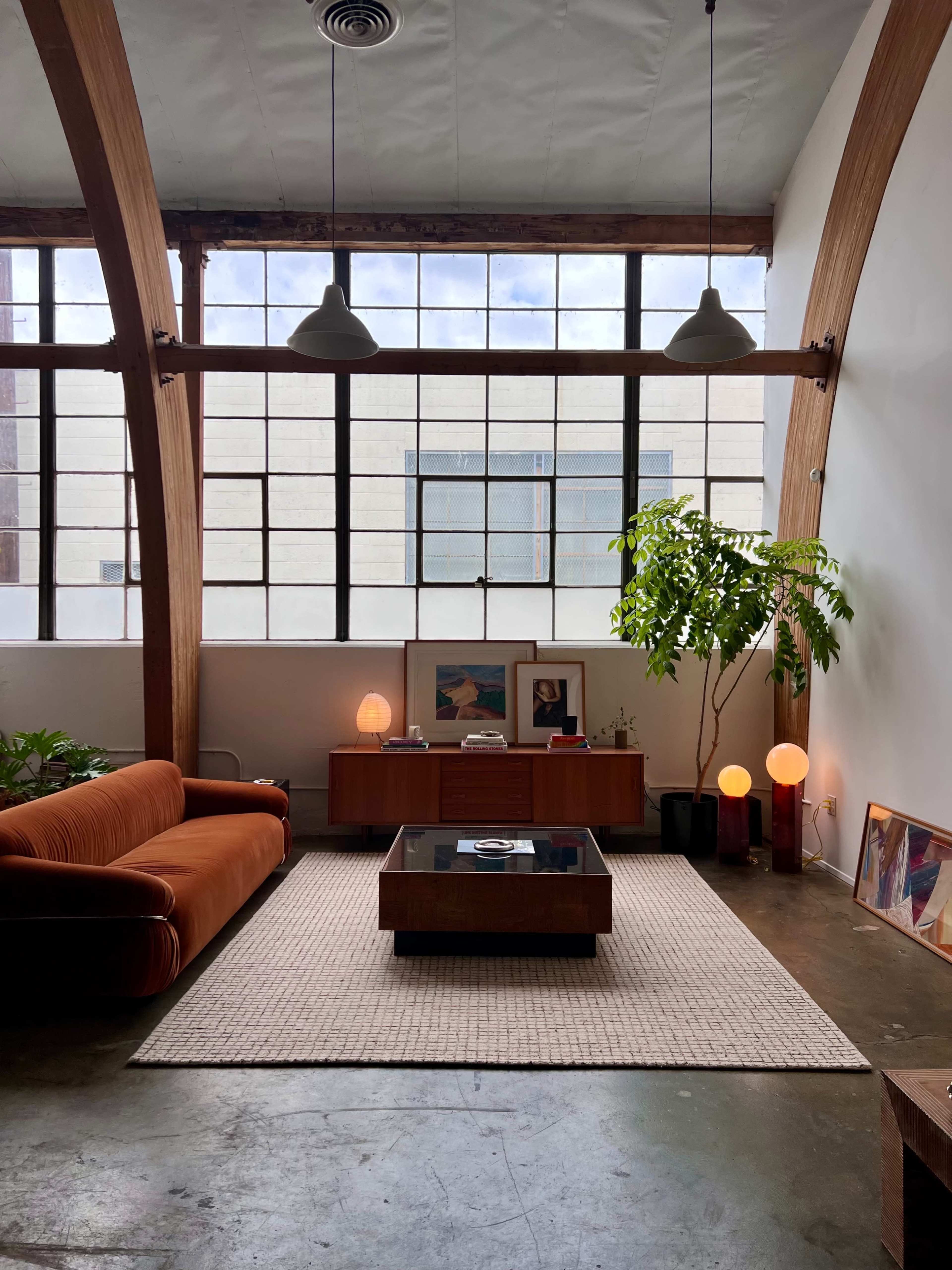 A modern living room with a large window, a brown sofa, a coffee table, a rug, and potted plants.
