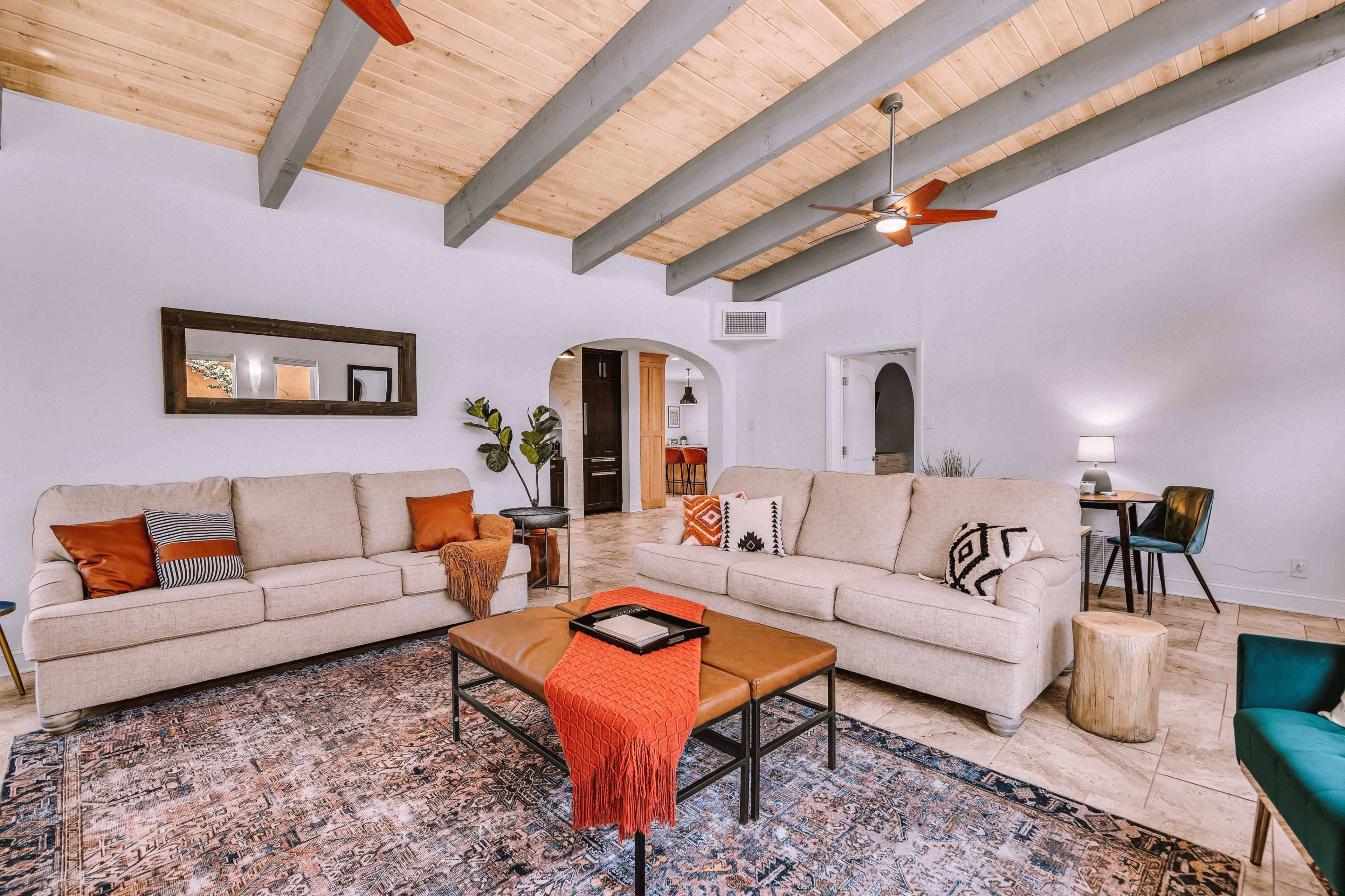 A cozy living room with two sofas facing a wooden coffee table, featuring a patterned rug and exposed beam ceiling.