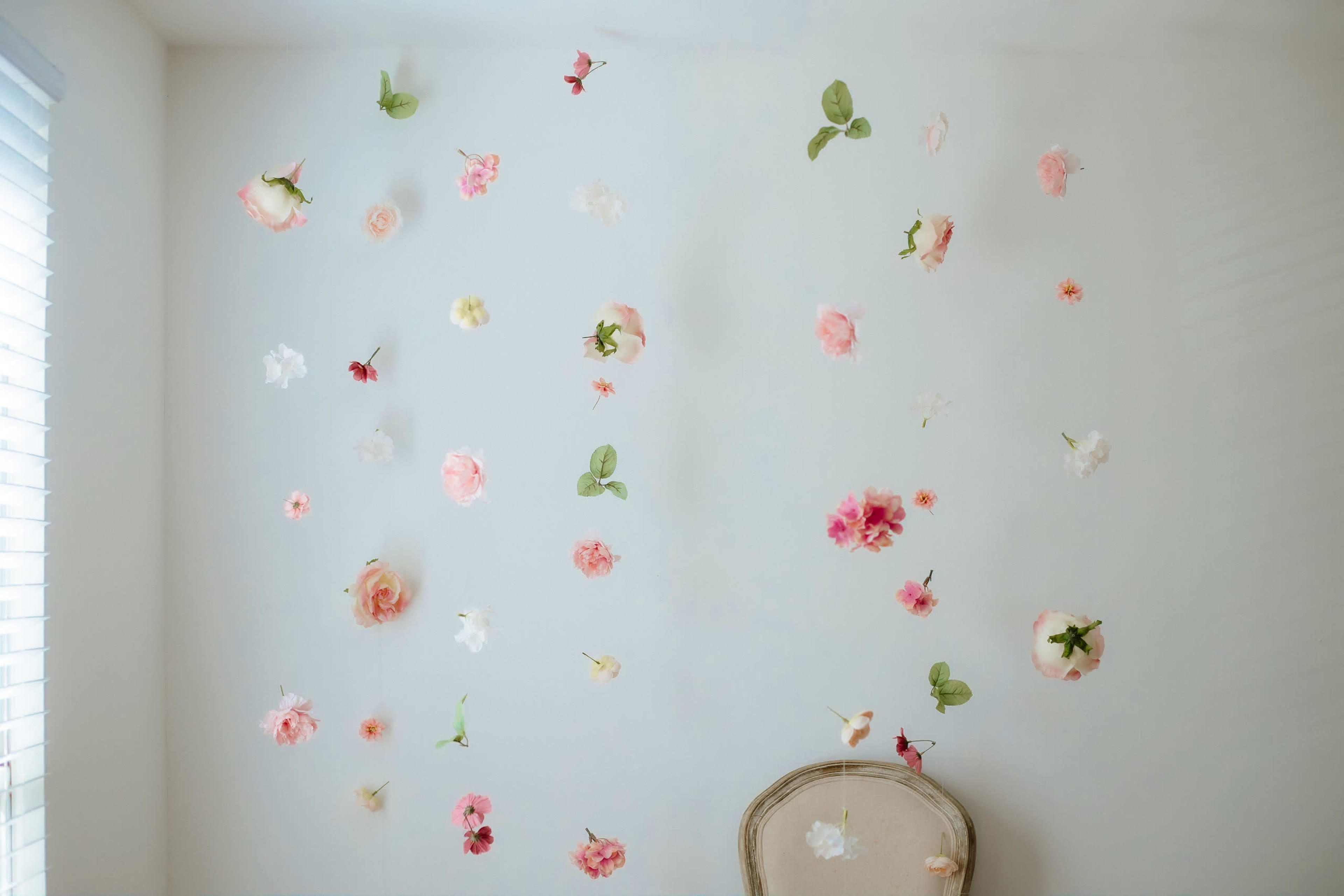 A light-colored wall is decorated with a variety of faux flowers and leaves, while a vintage chair sits at the bottom.