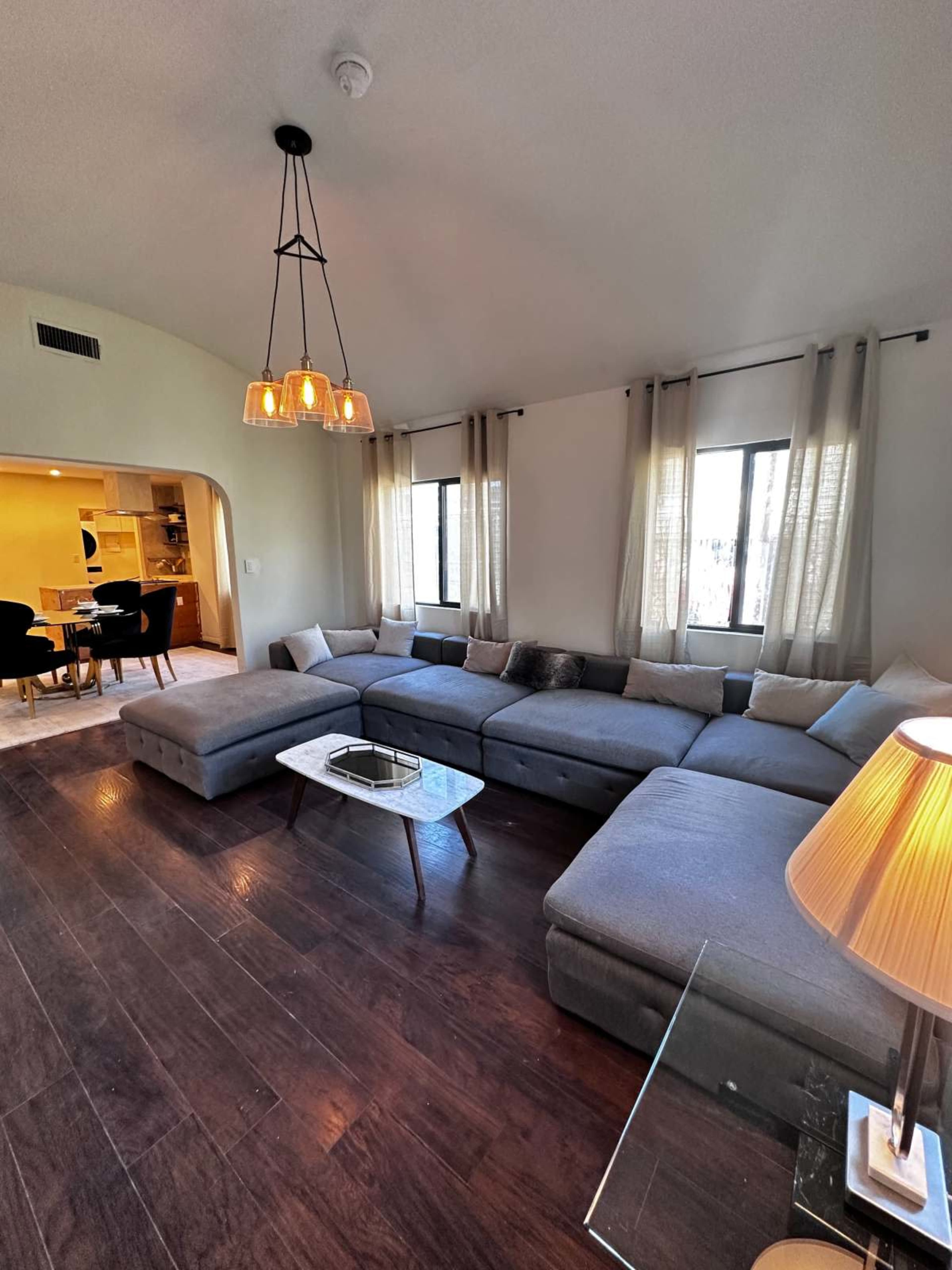 The image shows a modern living room with a large sectional sofa, a coffee table, and a pendant light hanging from the ceiling.