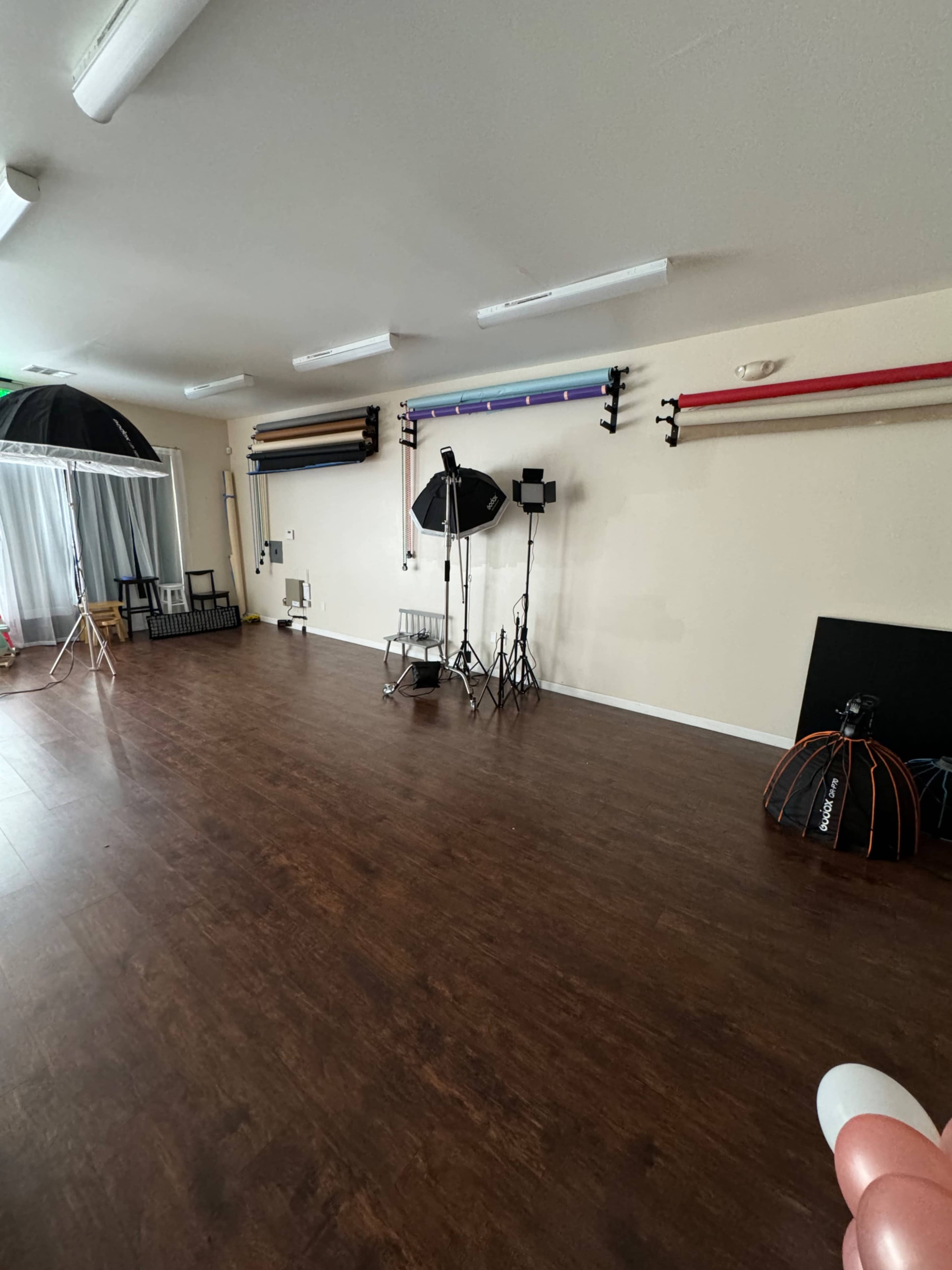 A photography studio with backdrop support stands, lighting equipment, and a wooden floor.
