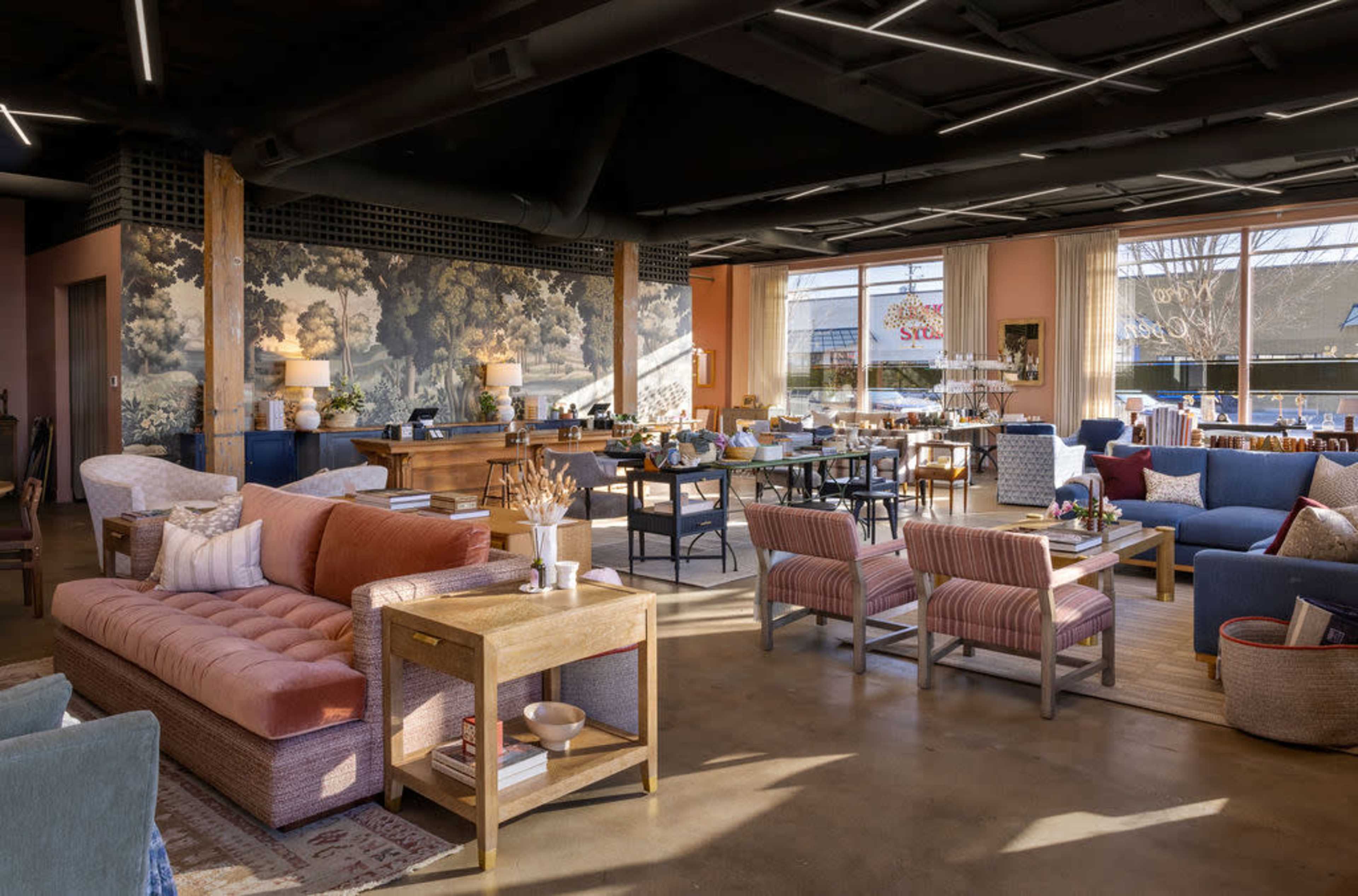 A spacious living area with a mix of seating including a large sectional sofa, various armchairs, and a dining table, all set against a backdrop of large windows and decorative wall art.