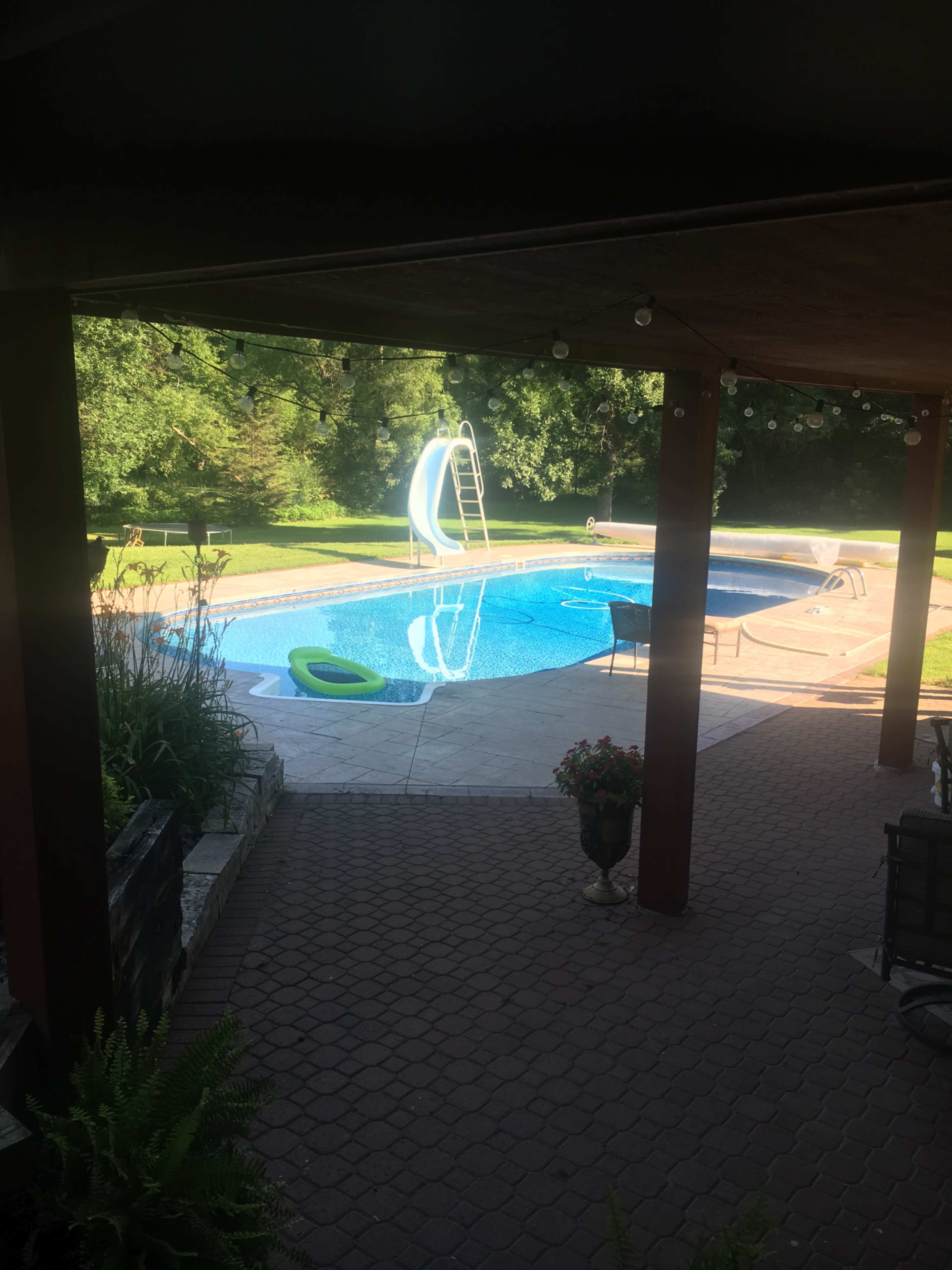 A swimming pool with a slide is surrounded by greenery and a patio area with seating.
