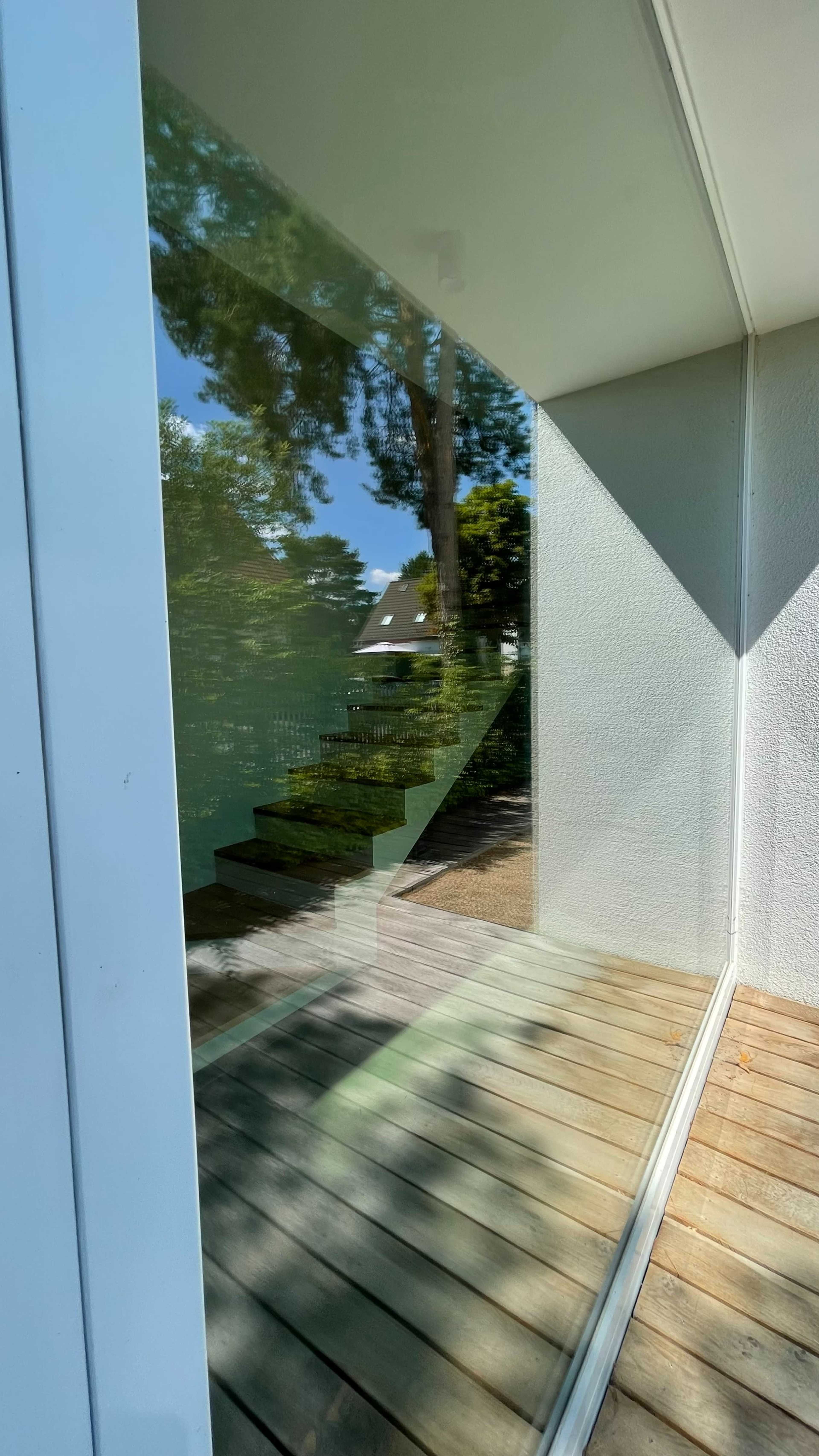 A glass surface reflecting a staircase and trees outside a modern building.
