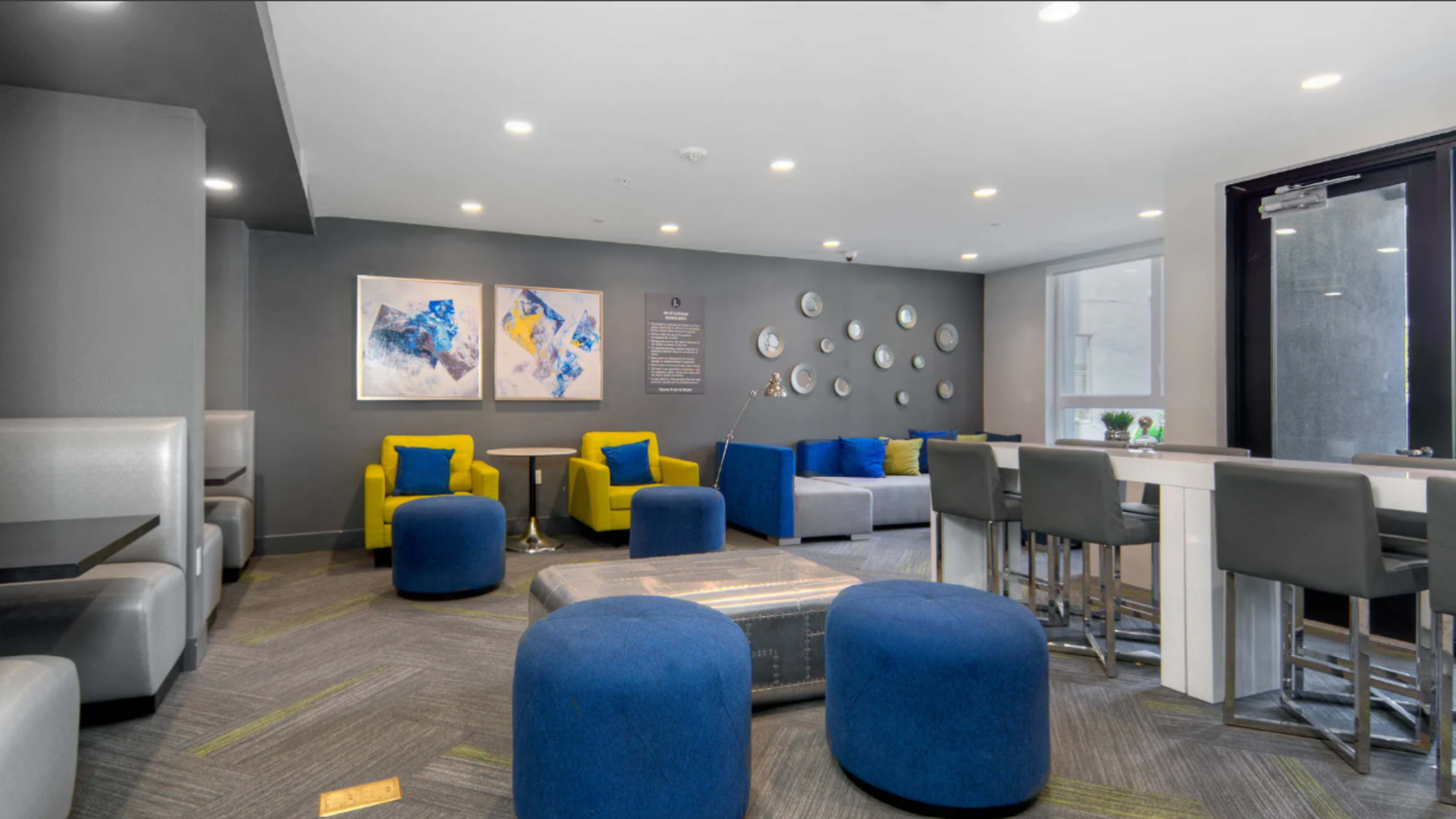 The image shows a modern lounge area featuring gray walls, colorful seating, and decorative wall art.