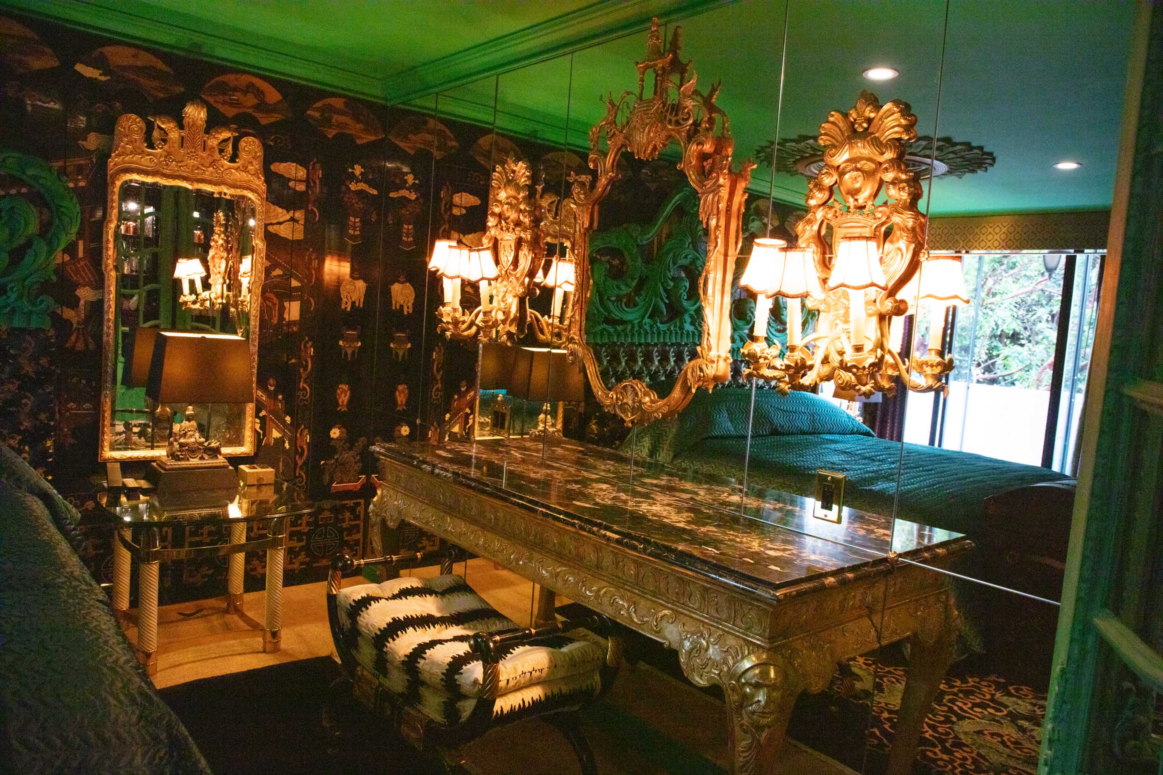 The scene depicts a lavishly decorated bedroom featuring mirrored walls, an ornate desk with a black marble top, and a chandelier with multiple lamps, all set against a green color scheme.