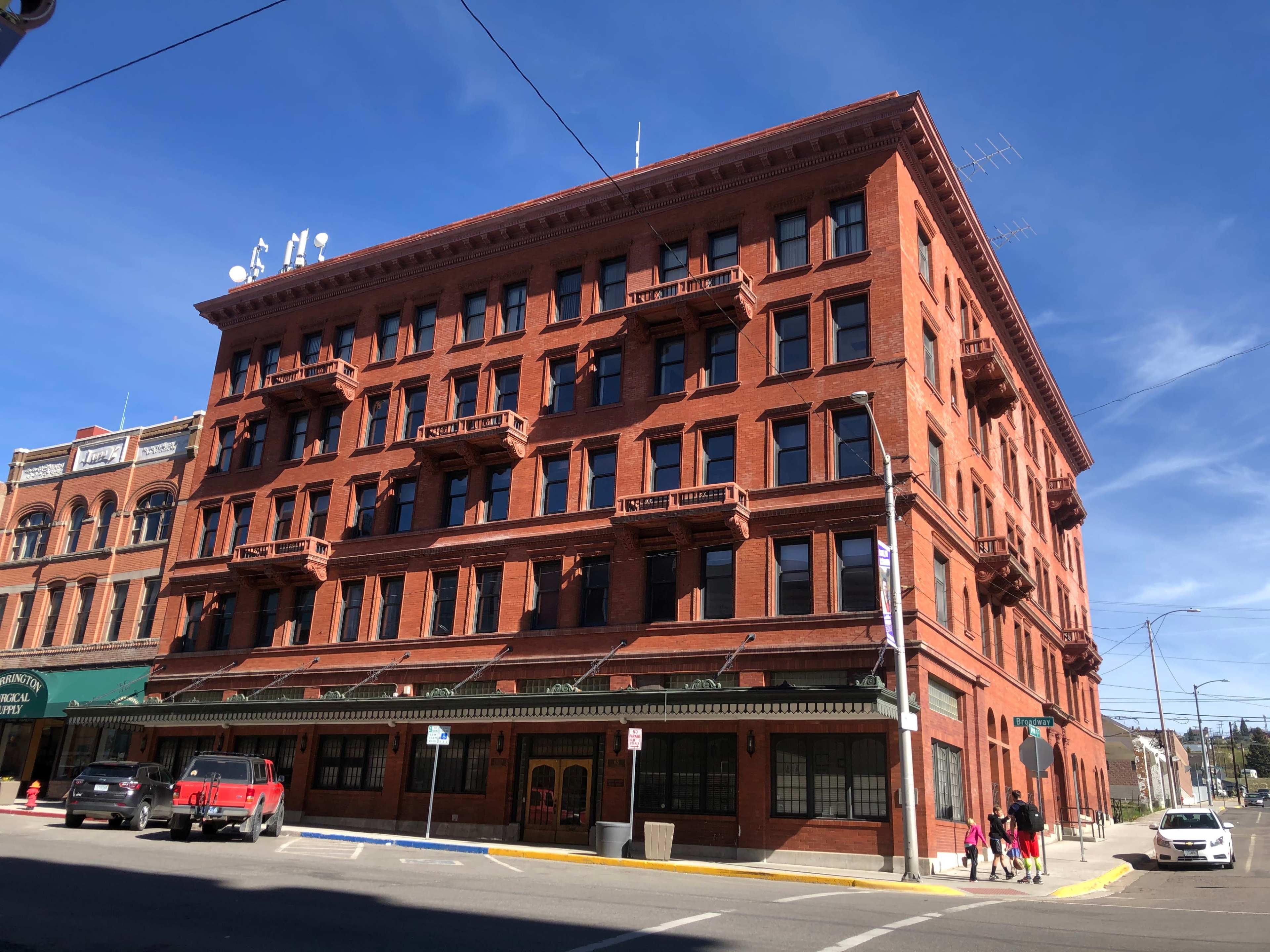 A large red brick building with multiple windows and balconies, located at a street corner.