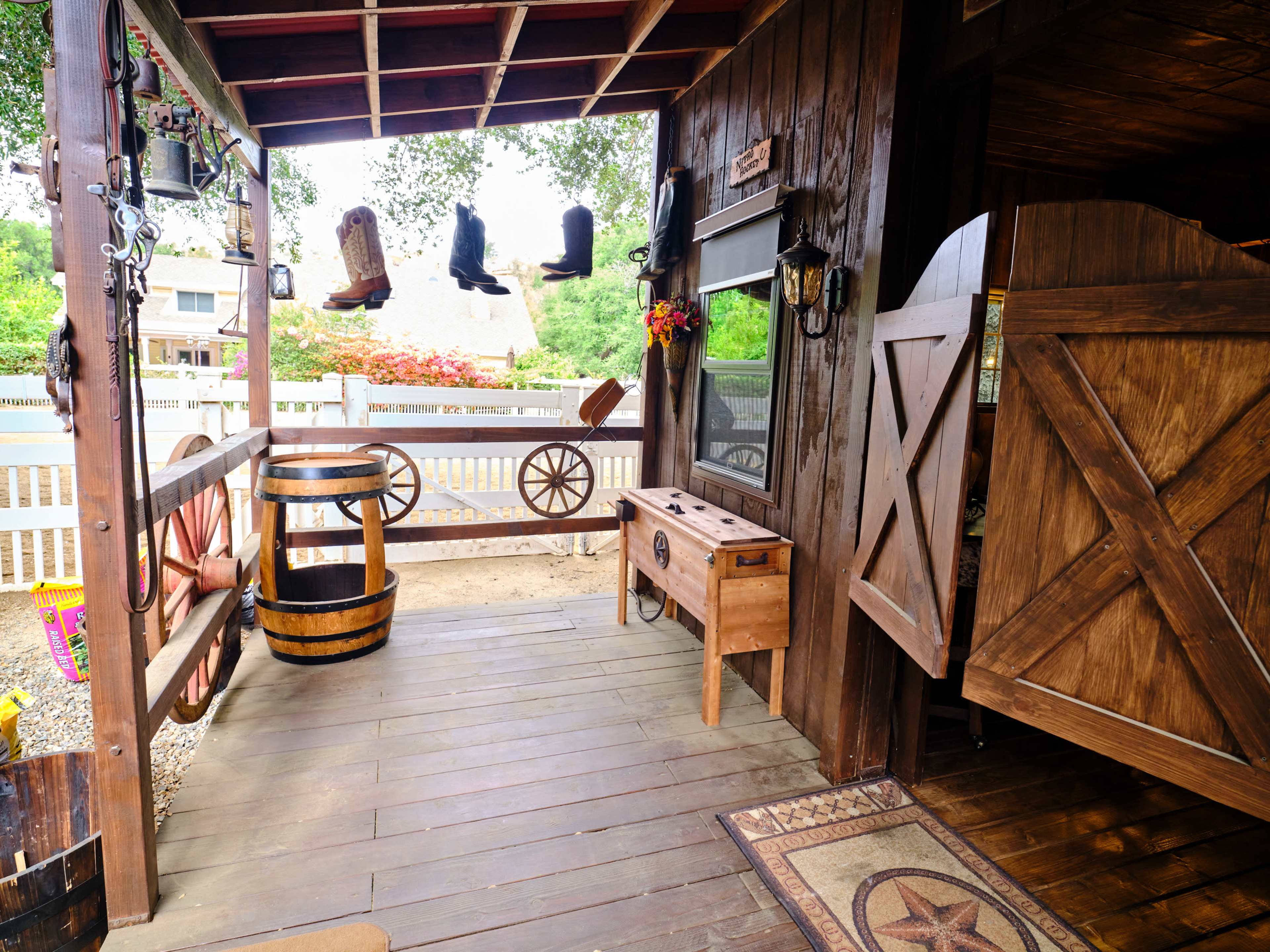 A rustic wooden porch with a barrel, a small table, and cowboy boots hanging from the ceiling.