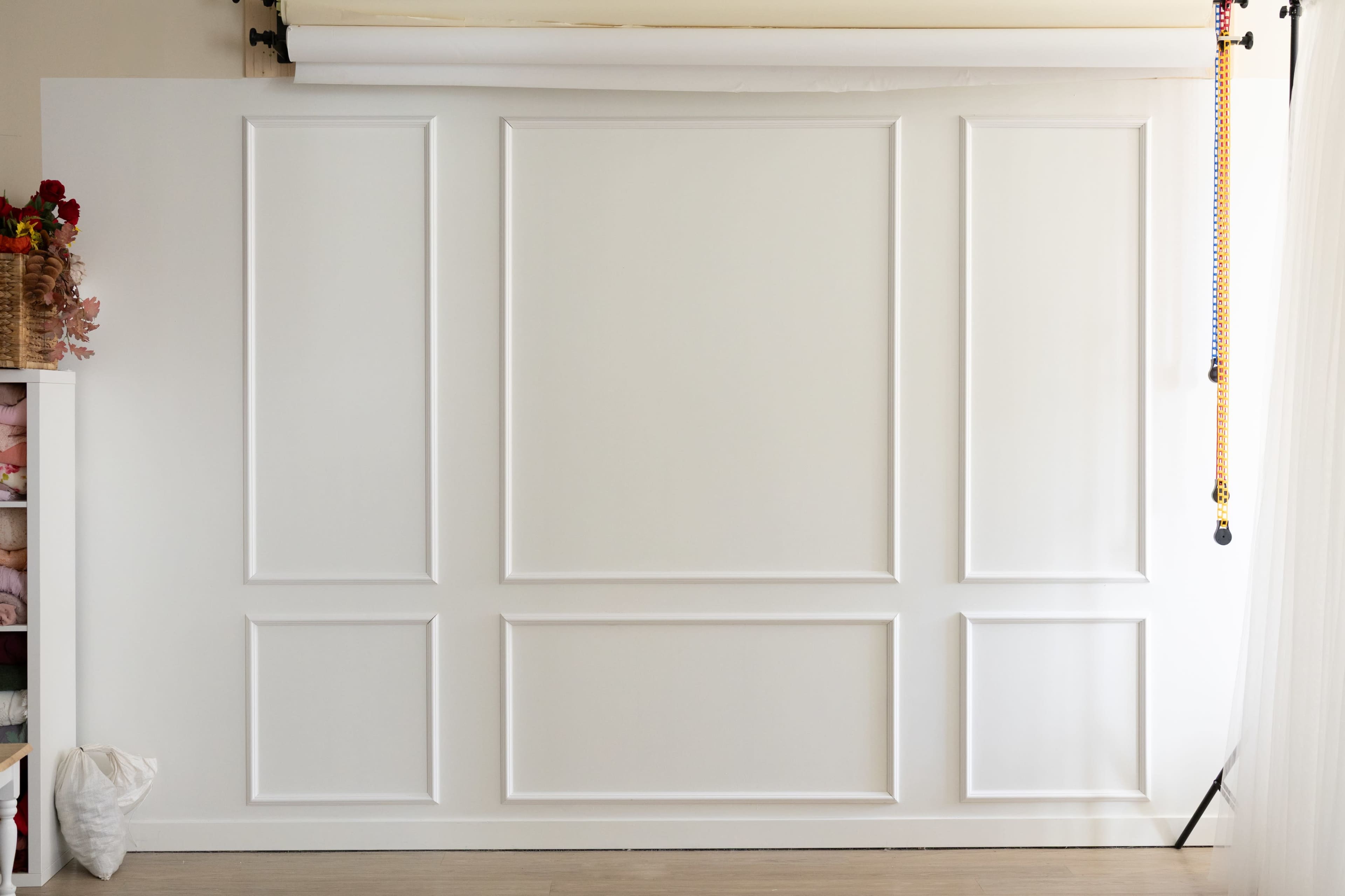 The image shows a plain white wall with a panel design and a roll of backdrop paper hanging above.