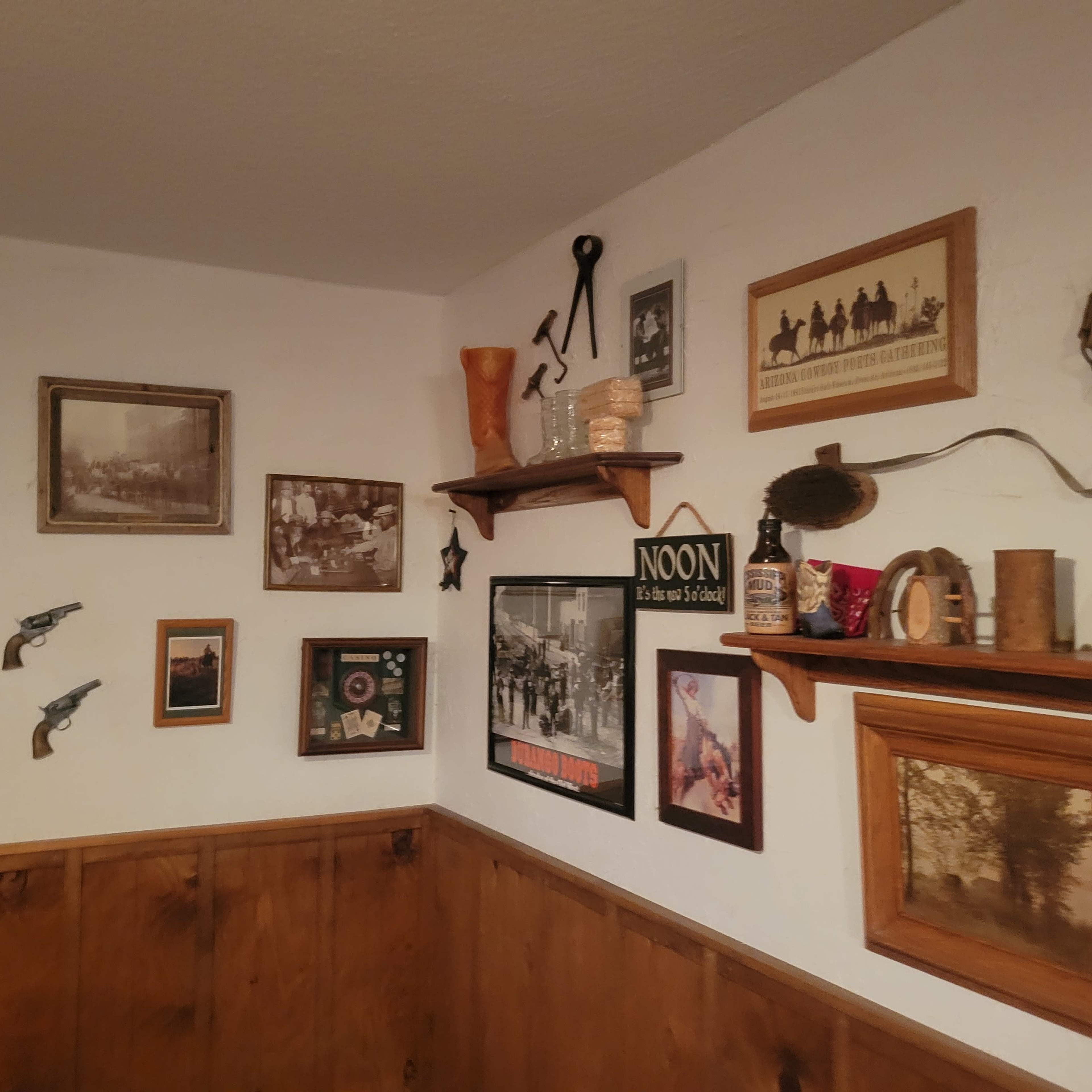 The image shows a corner of a room adorned with a collection of vintage photographs, wooden shelves, and rustic decor items on the walls.