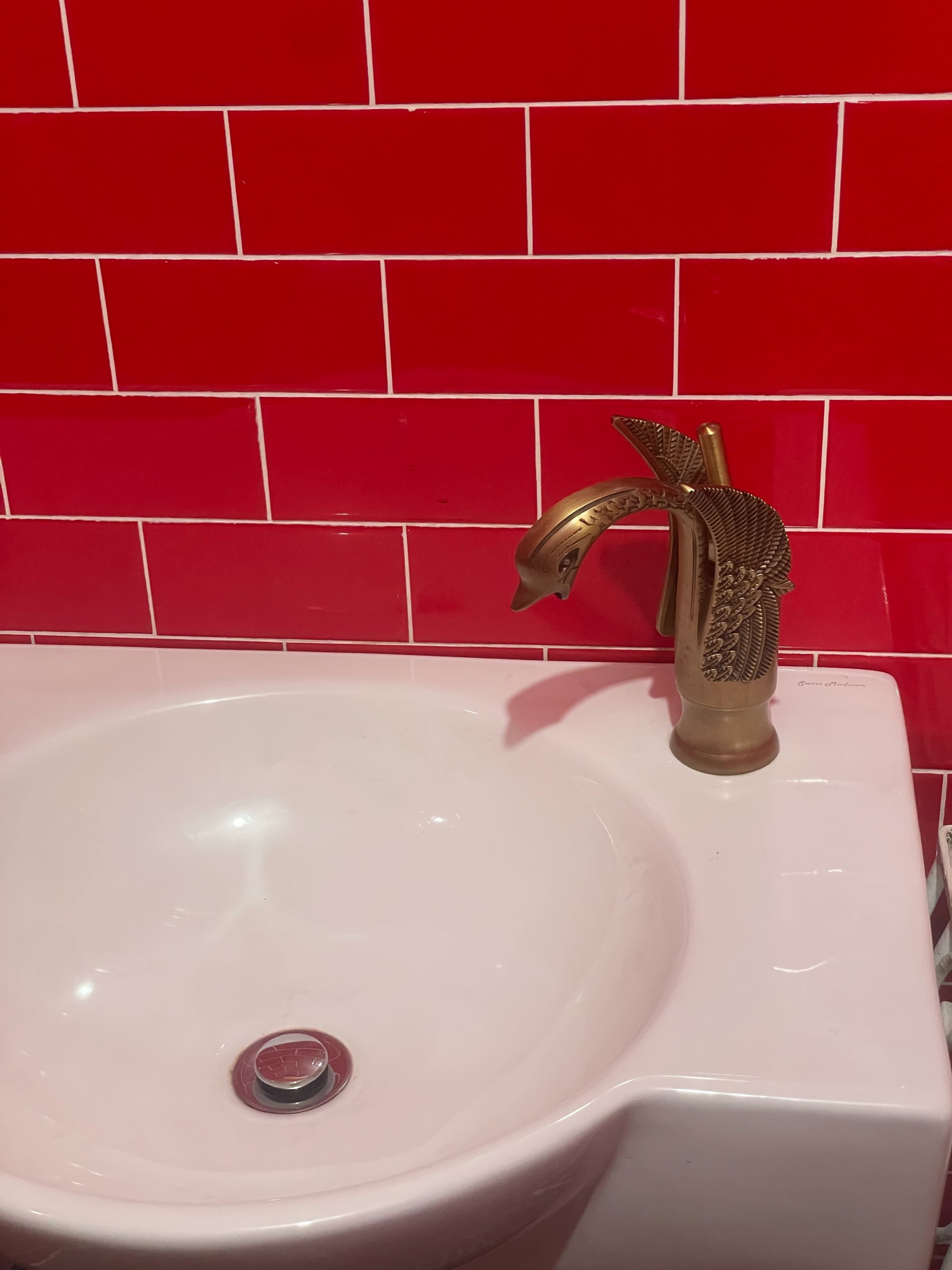 The image shows a white sink with a distinctive gold faucet shaped like a fish, set against a red tiled wall.