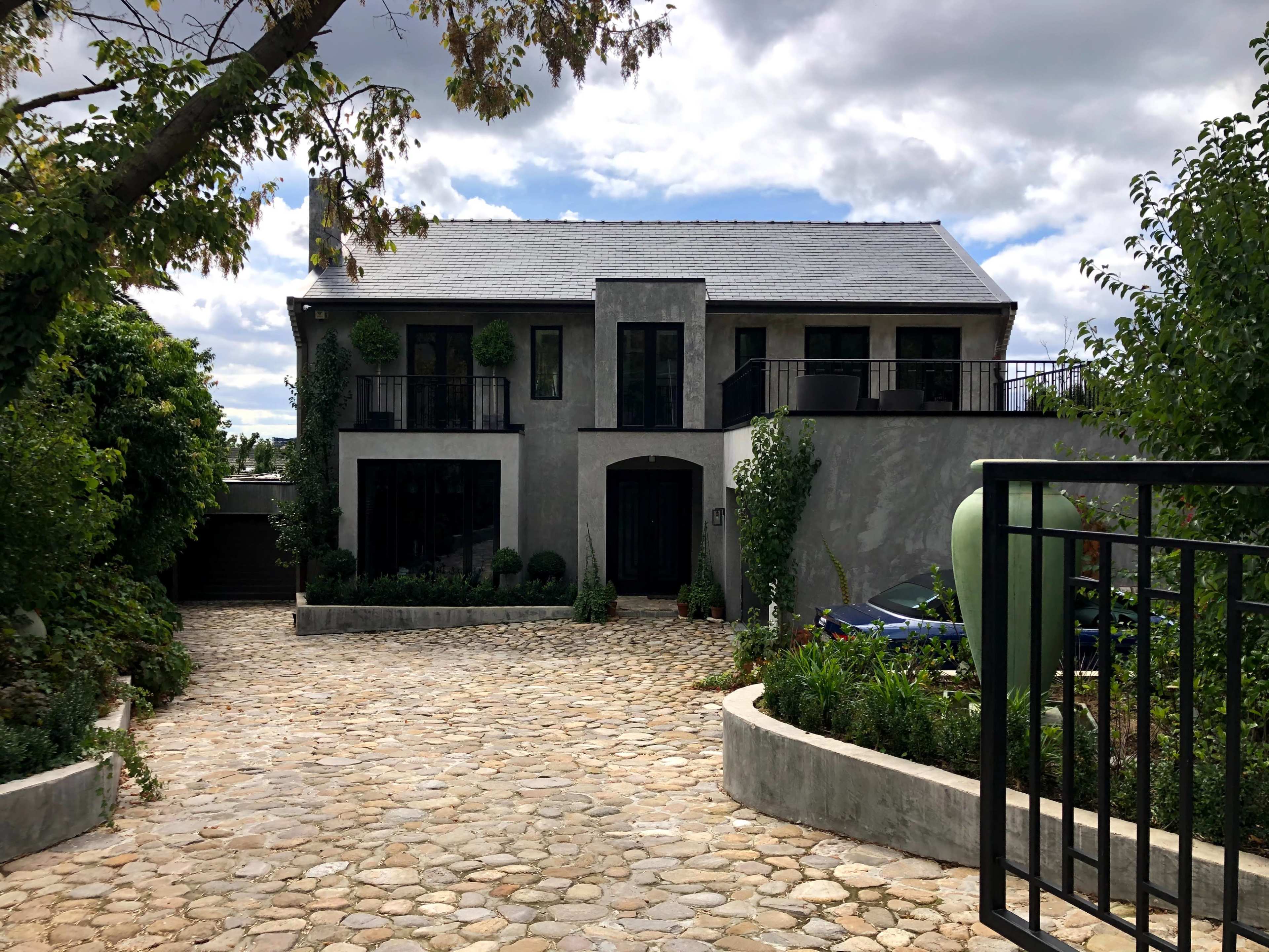 A modern two-story house with a gray exterior, a stone pathway leading to the entrance, and greenery surrounding the property.