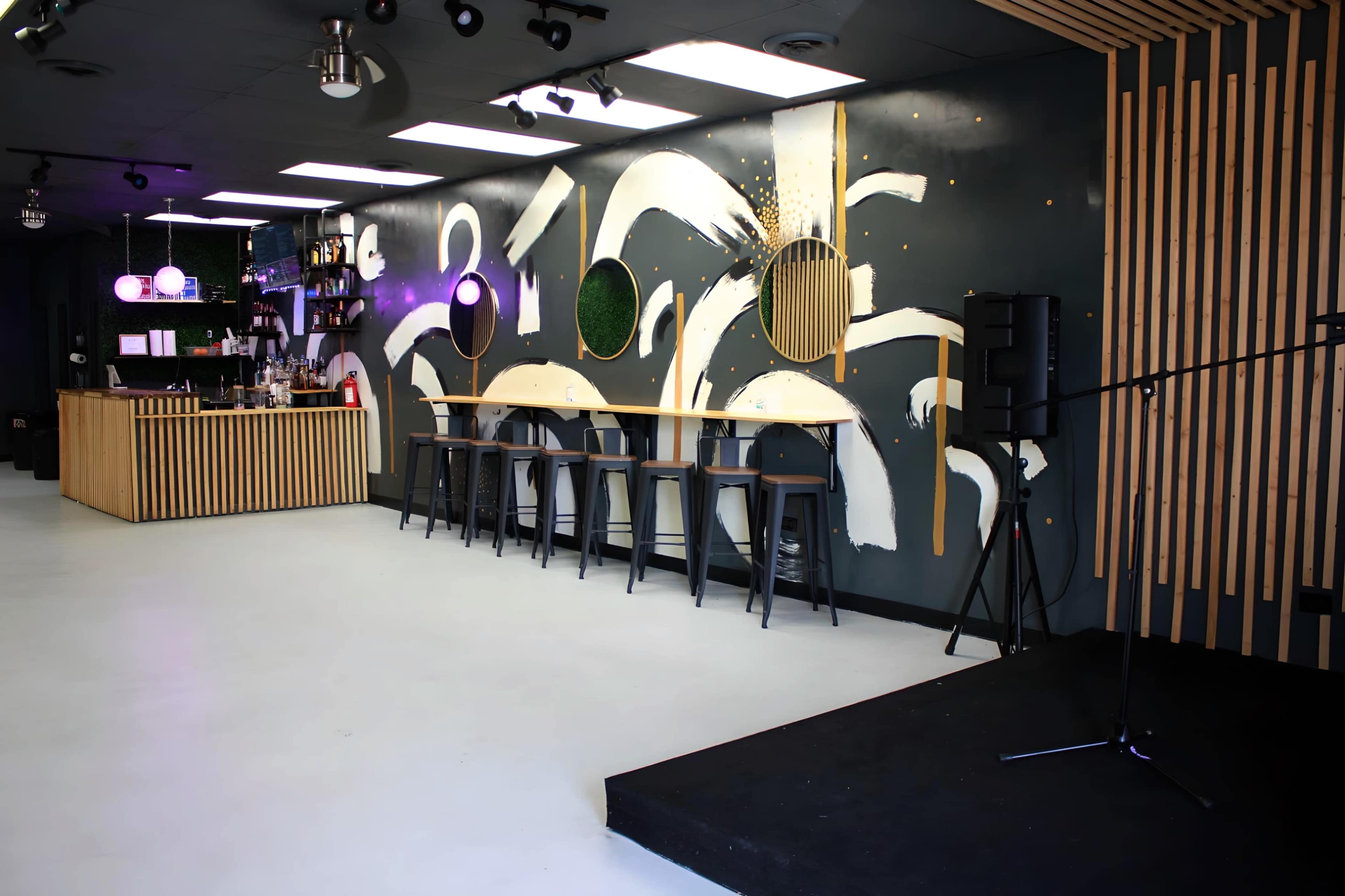 A modern cafe interior featuring a bar area, high stools, and a stage for performances, with abstract wall designs and wooden accents.